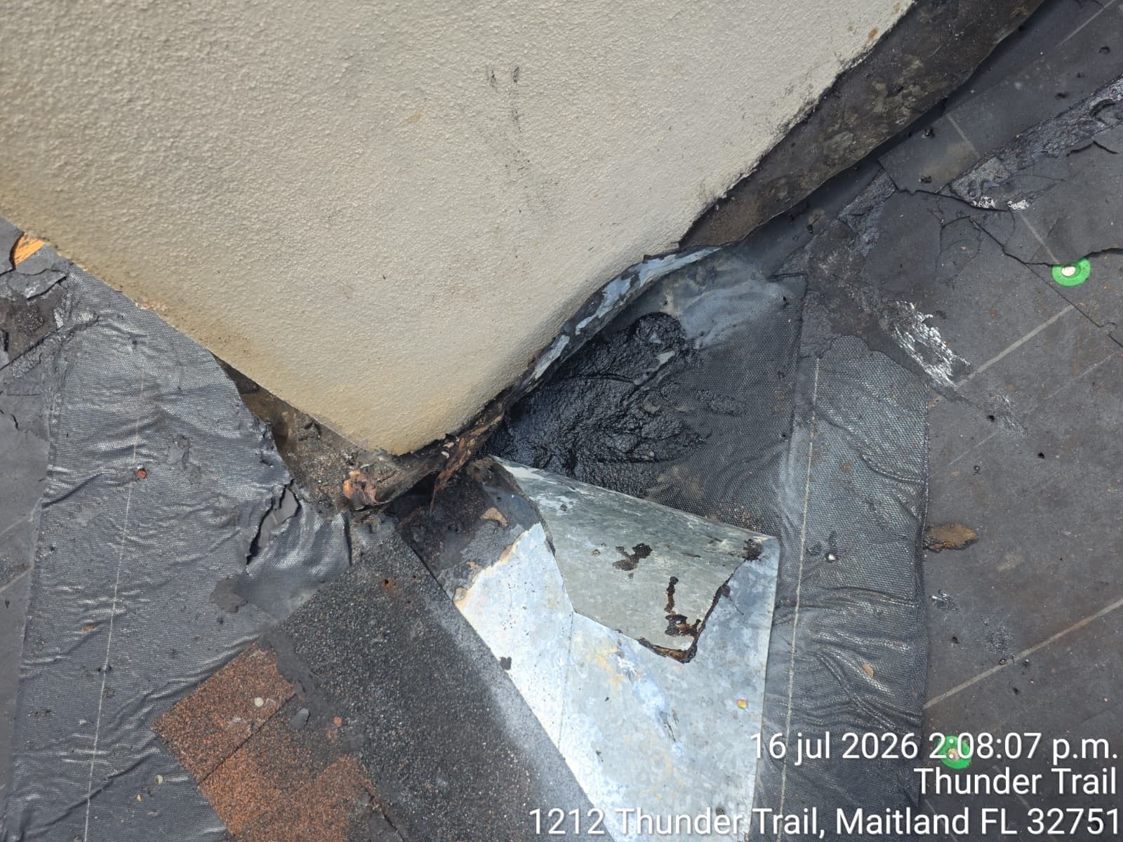 Damaged sidewalk curb with cracked concrete, black tar patch, and a chipped metal plate near a wall