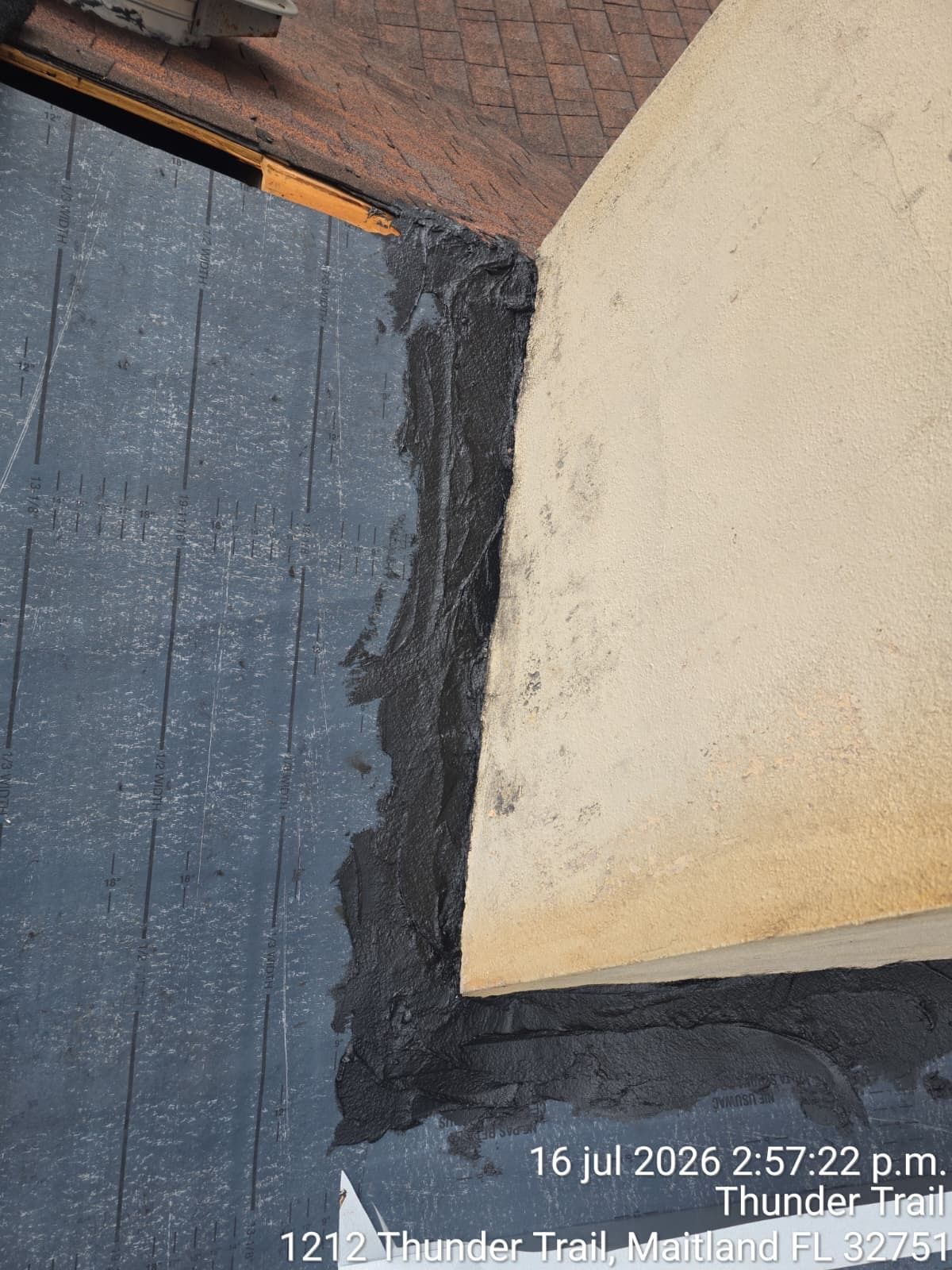 Close-up of a black roof edge meeting a beige wall and blue-gray shingle roof with dark sealant seam.