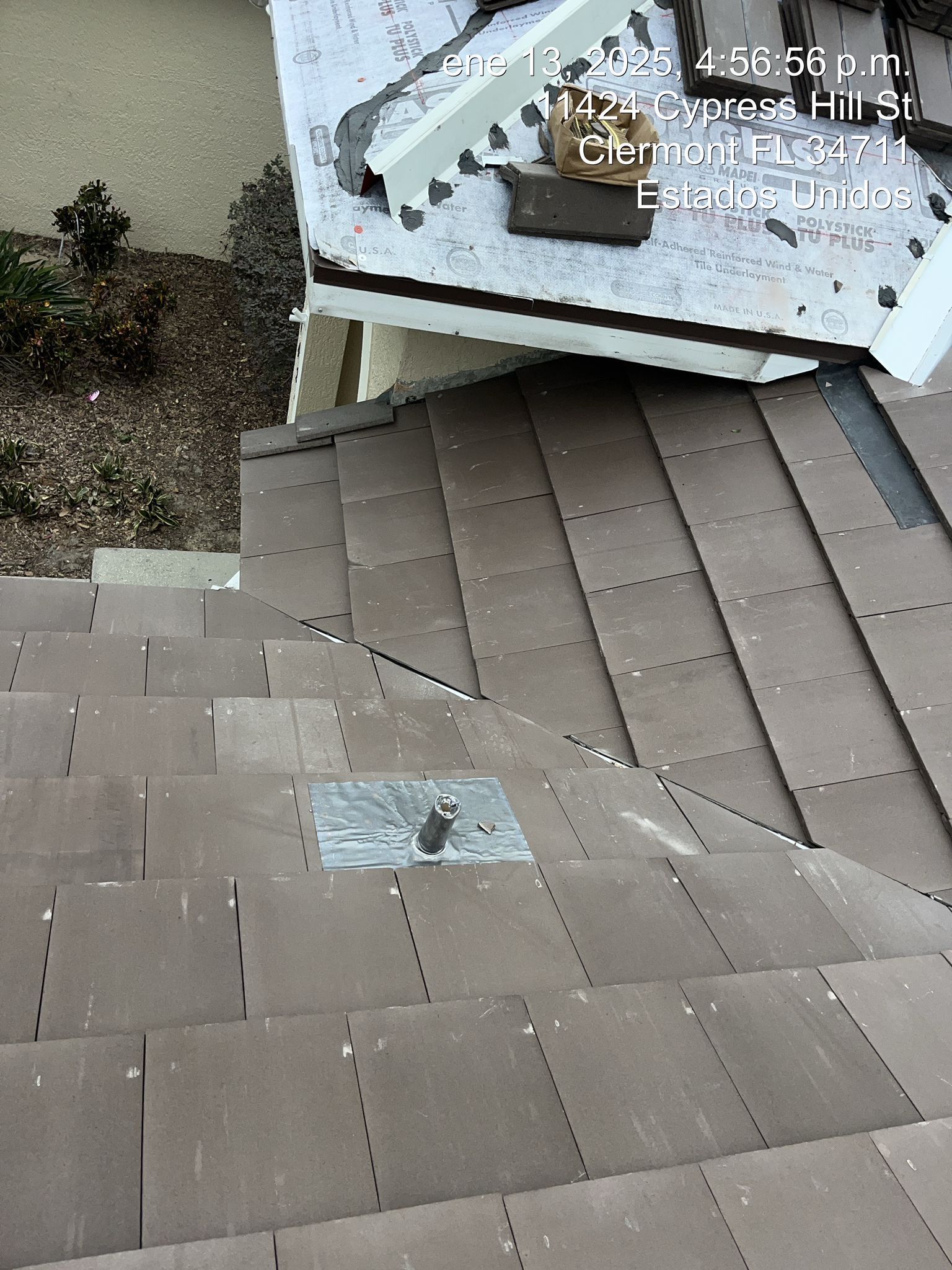 Roof shingles around a vent pipe with a damaged, torn edge near the roof trim