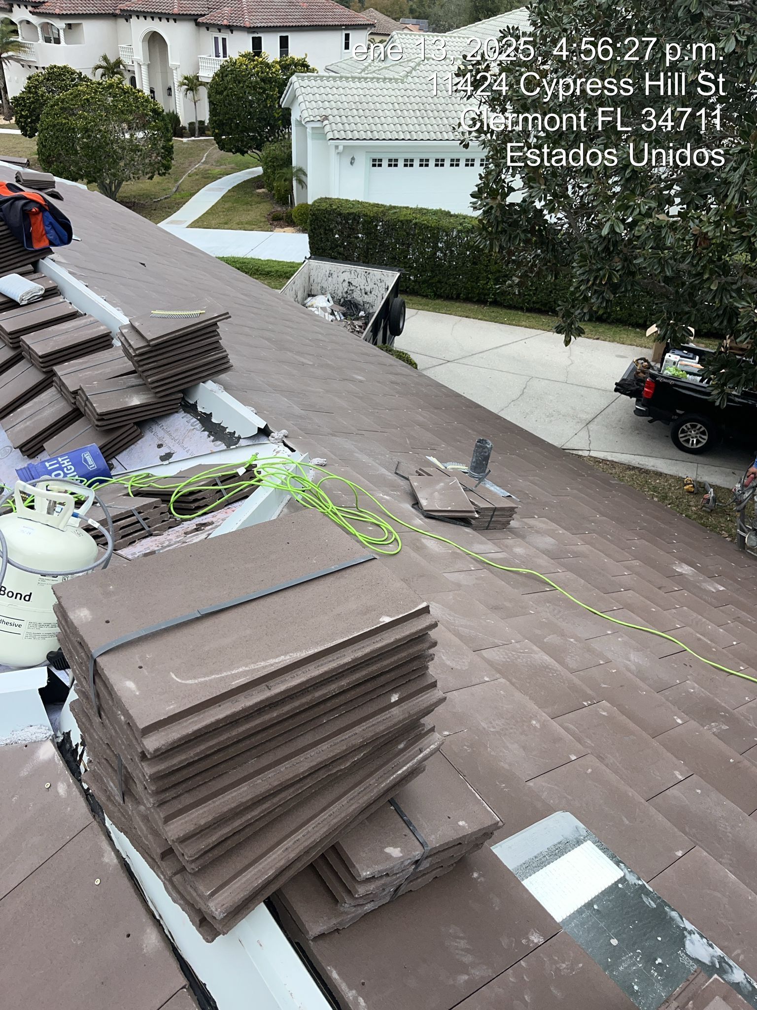 Rooftop with stacked tiles and tools beside a sloped driveway in a residential neighborhood