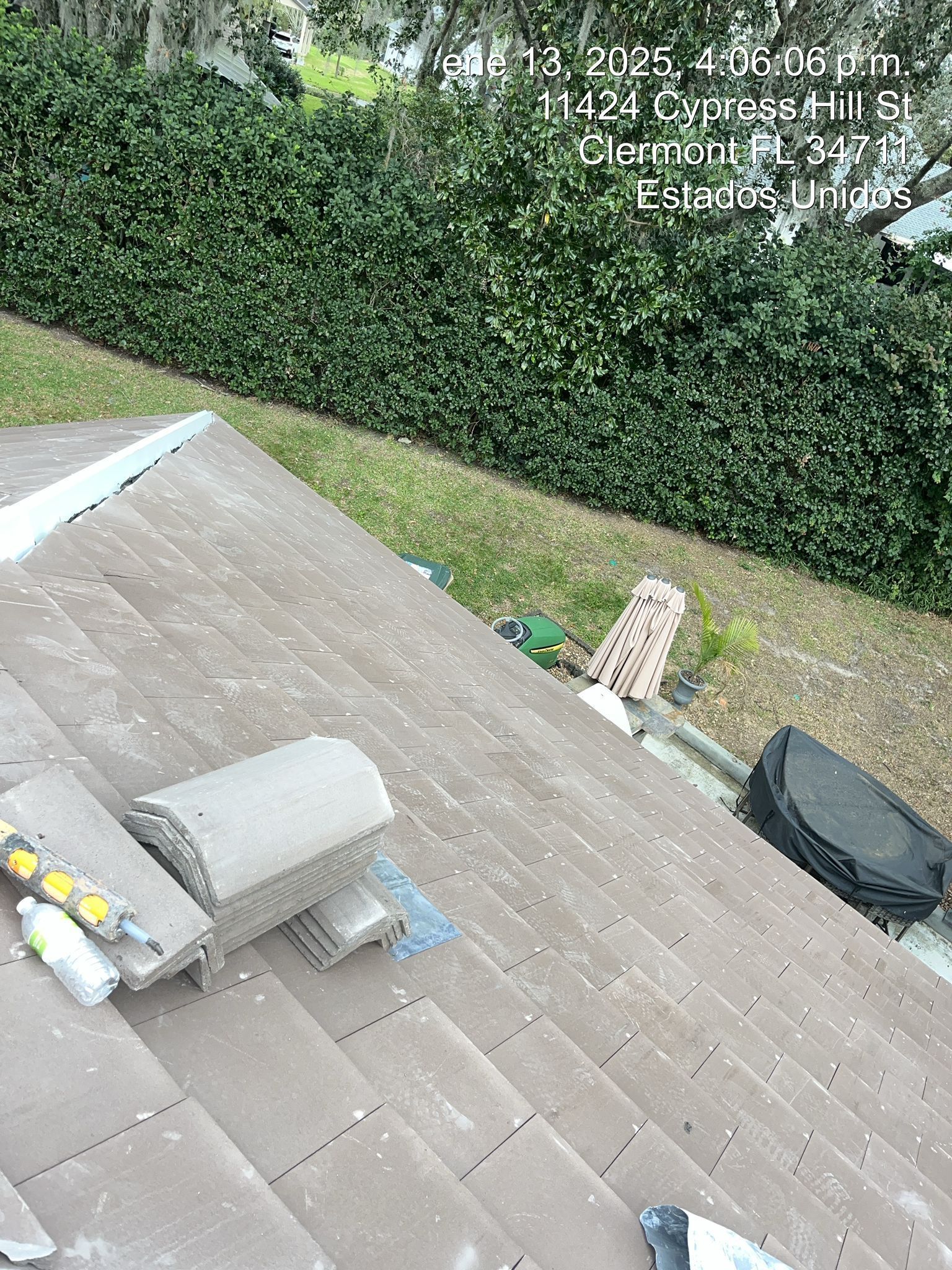Roof with shingles, skylight, and tools beside a tall hedge and lawn below