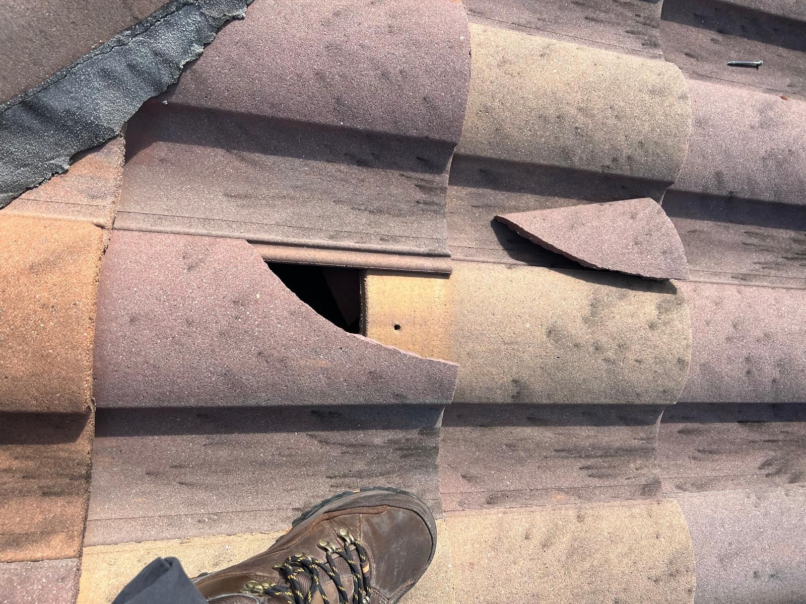 Damaged roof shingles with a hole and a boot on the roof edge