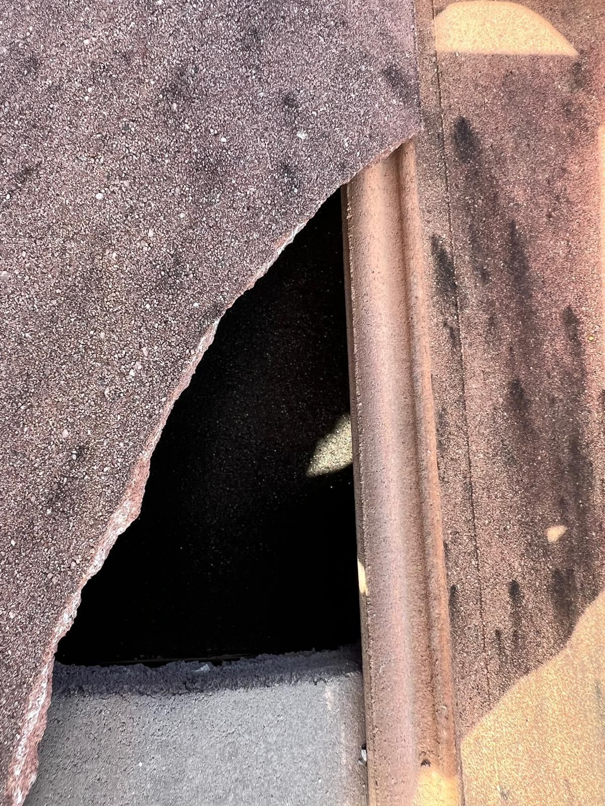 Close-up of a weathered metal surface with a dark opening and a vertical pipe beside it.