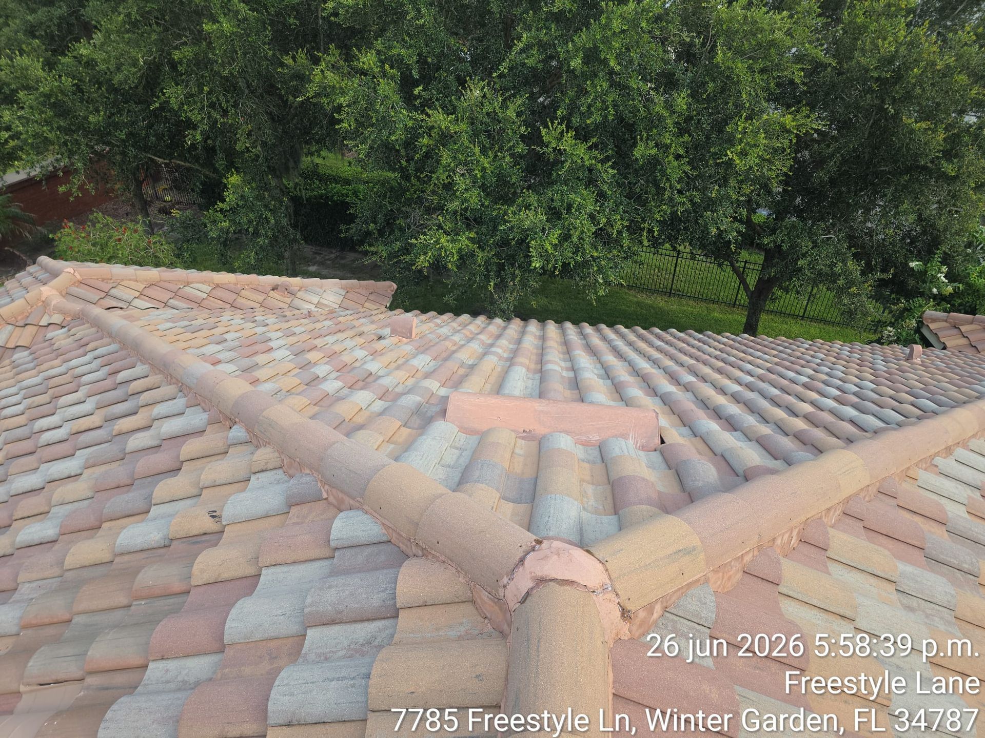 Rooftop view of tan barrel tile shingles with trees in the background