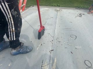 Person sweeping debris from a concrete surface with a red broom and dustpan