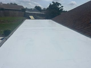 White roof under construction beside houses, with a sloped shingle roof and cloudy sky.