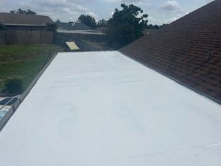 White roof deck beside a brown shingled roof, with trees and houses in the background
