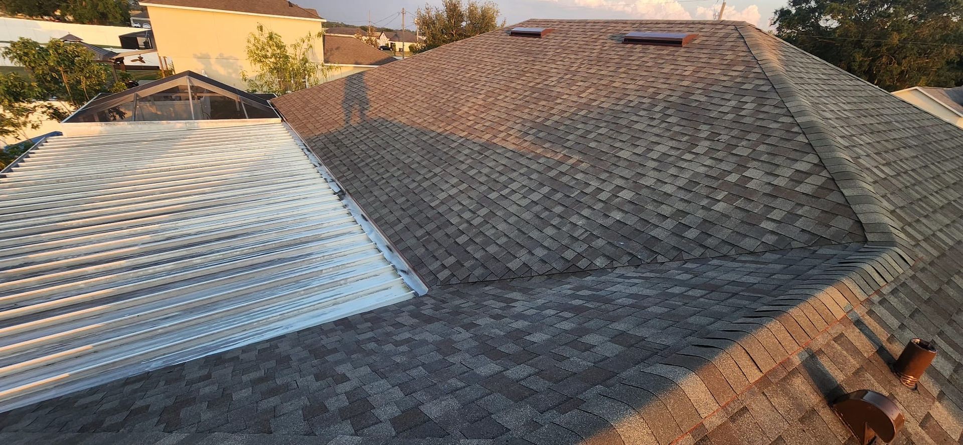 Sunlit roof with patched shingles and a large section covered in reflective white underlayment
