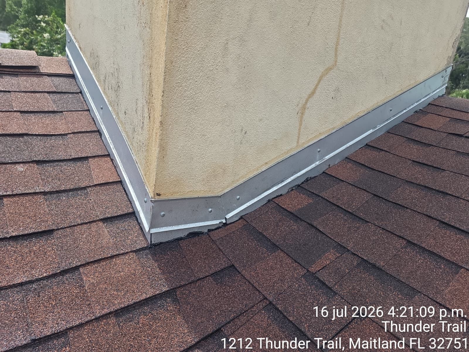 Roof shingles and metal flashing around a stucco chimney corner on a house exterior