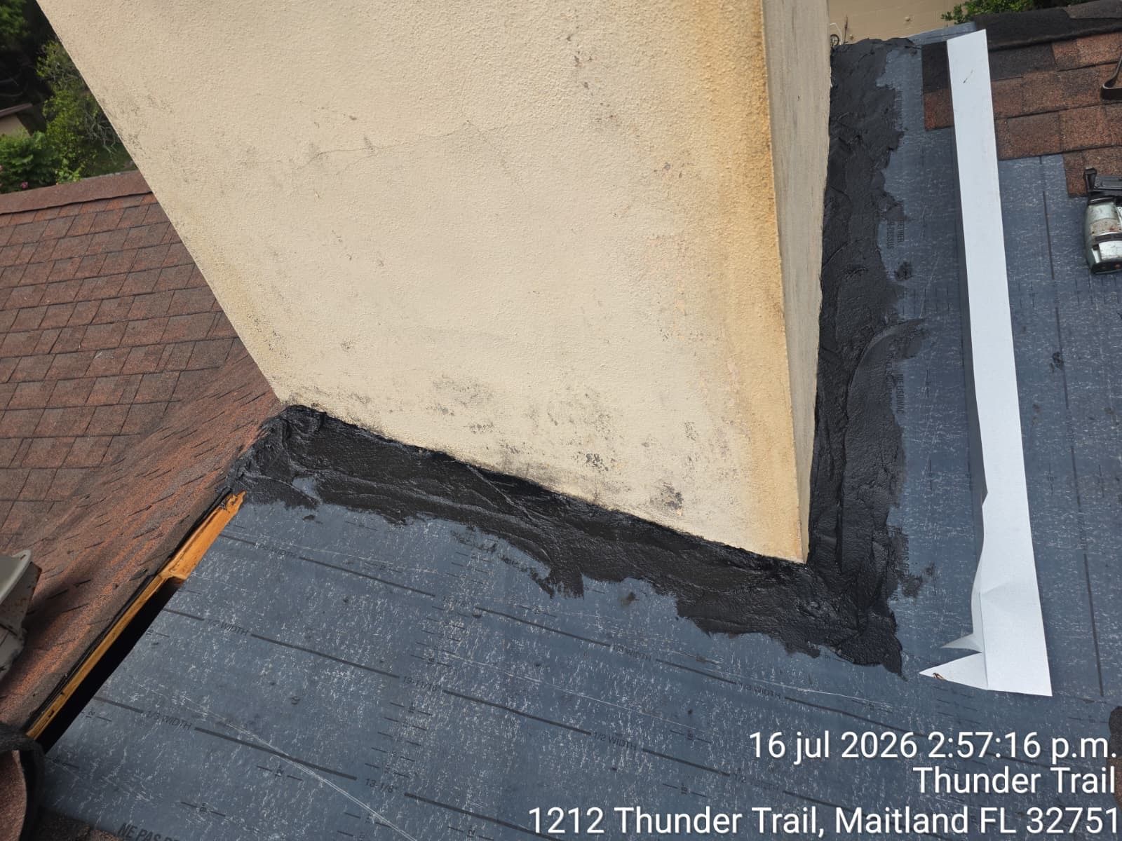 Roof flashing and black sealant around a beige chimney on a shingled rooftop.