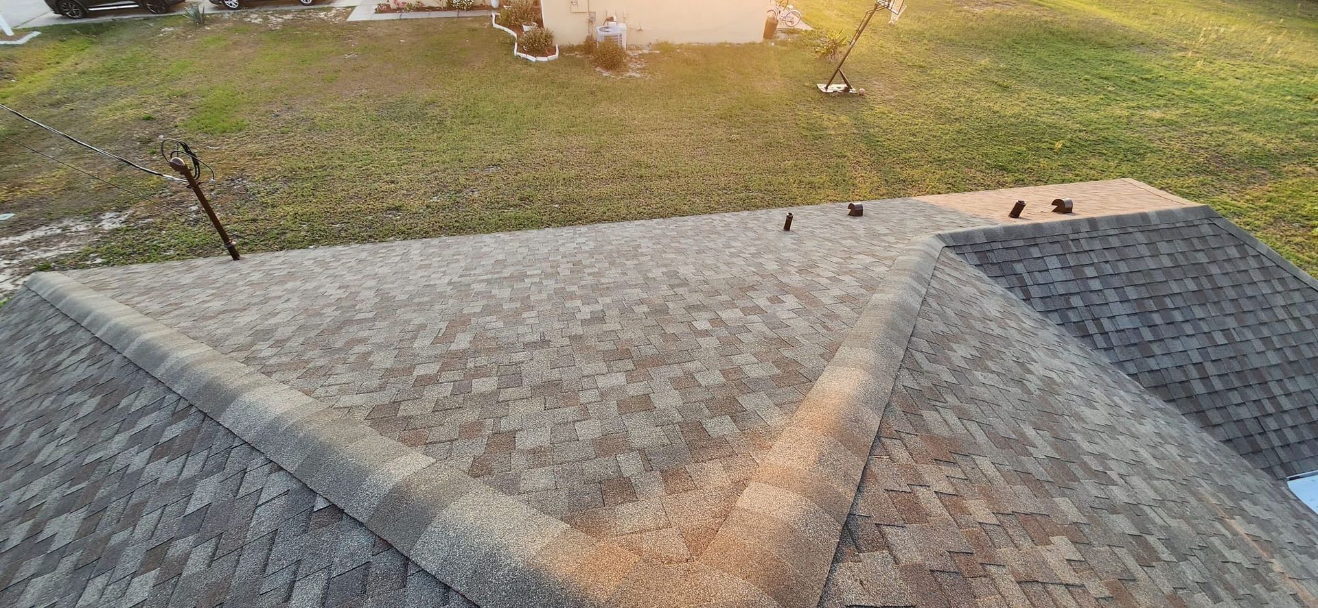 Roof shingles with a triangular shadow, overlooking a grassy yard at sunset.
