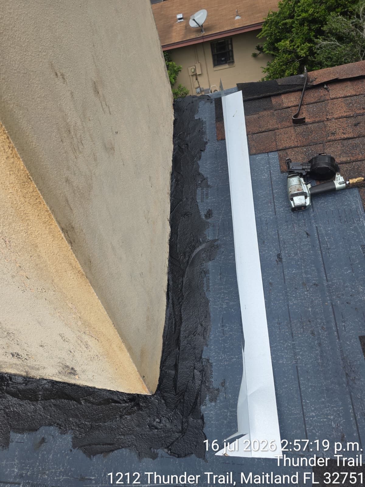 Rooftop view of a tan wall edge and dark roofing, with a nearby brick building and vents below.