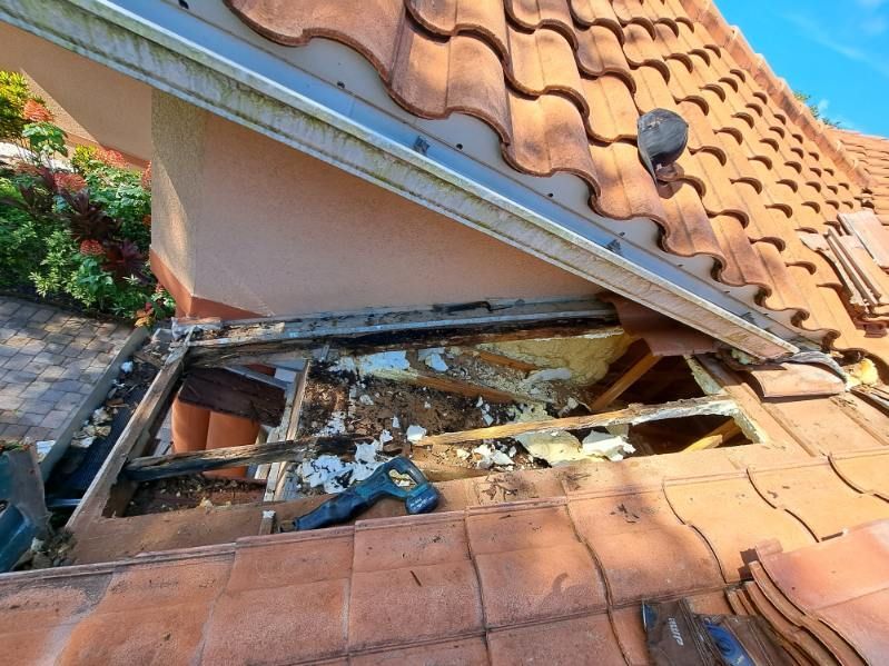 Damaged rooftop with a large hole exposing debris and wooden beams beneath orange roof tiles