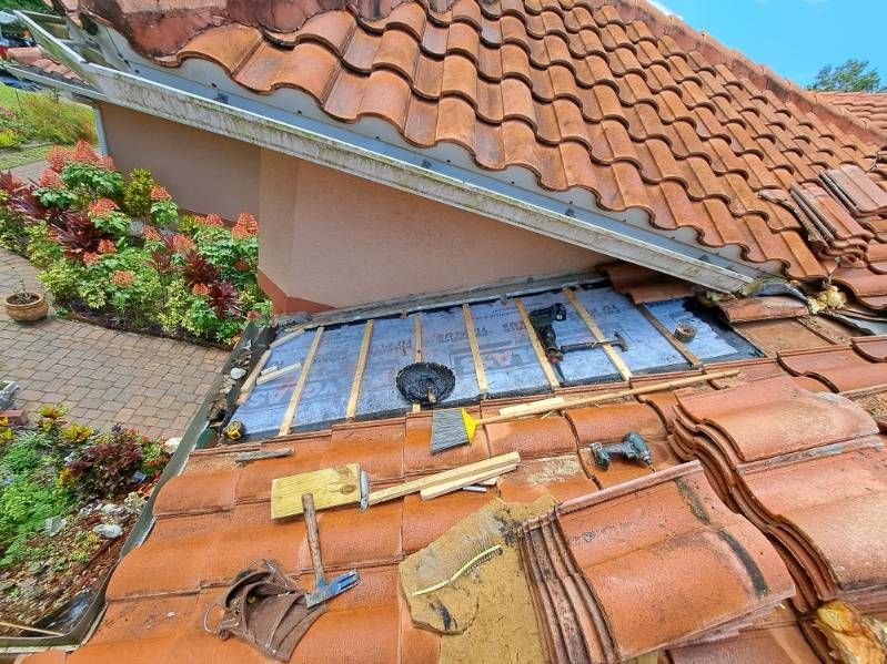 Damaged terracotta roof with a broken skylight and solar panels amid orange tiles and plants