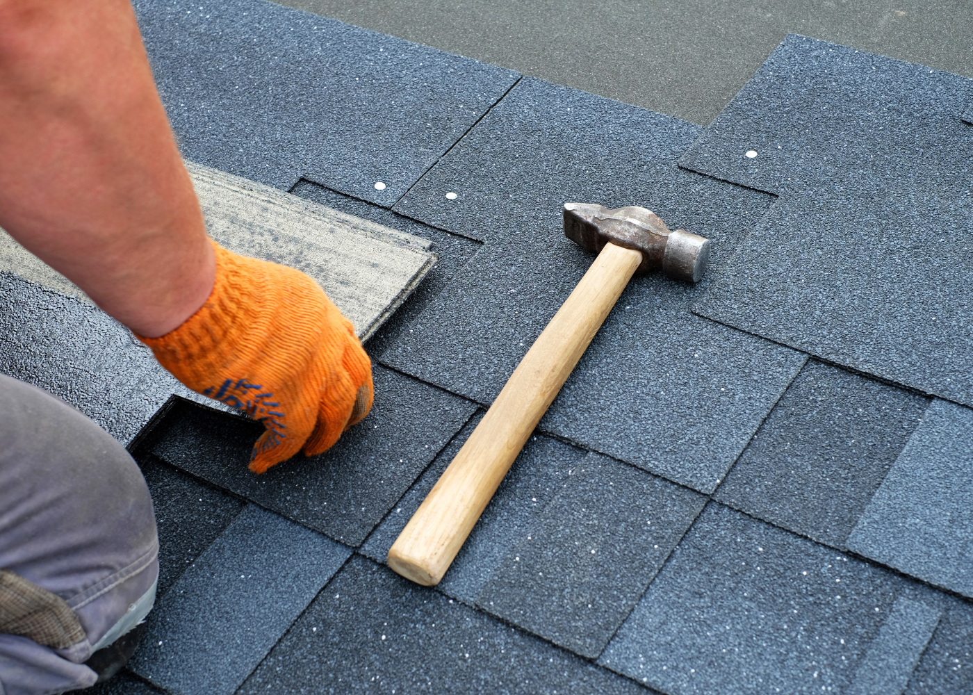 A person is installing shingles on a roof with a hammer.
