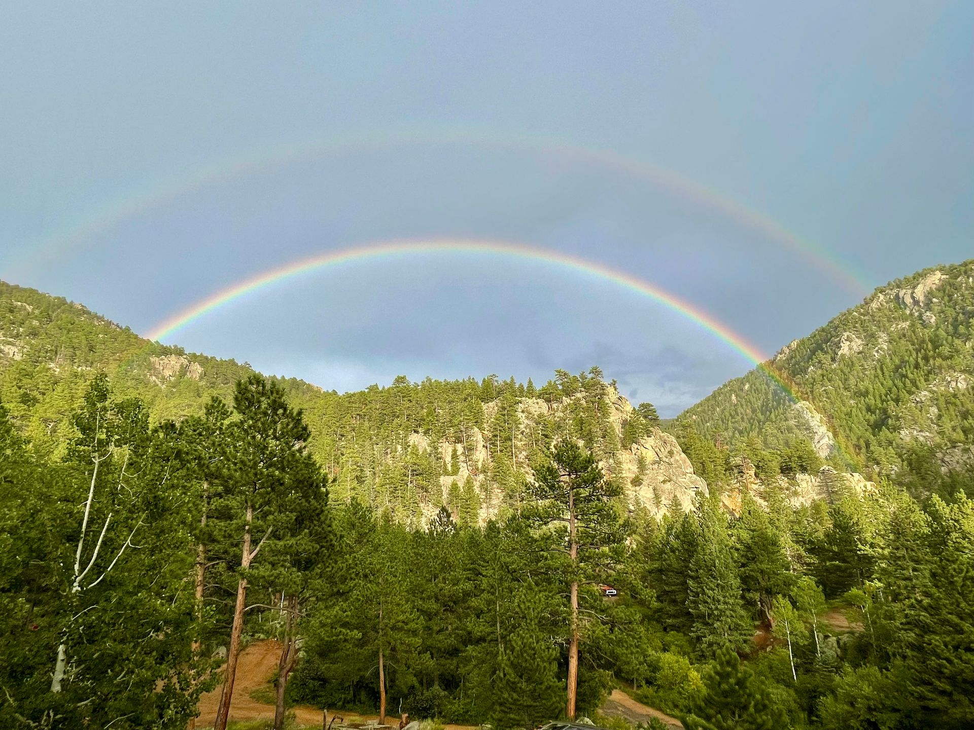 Double rainbow arches over lush green mountain range.