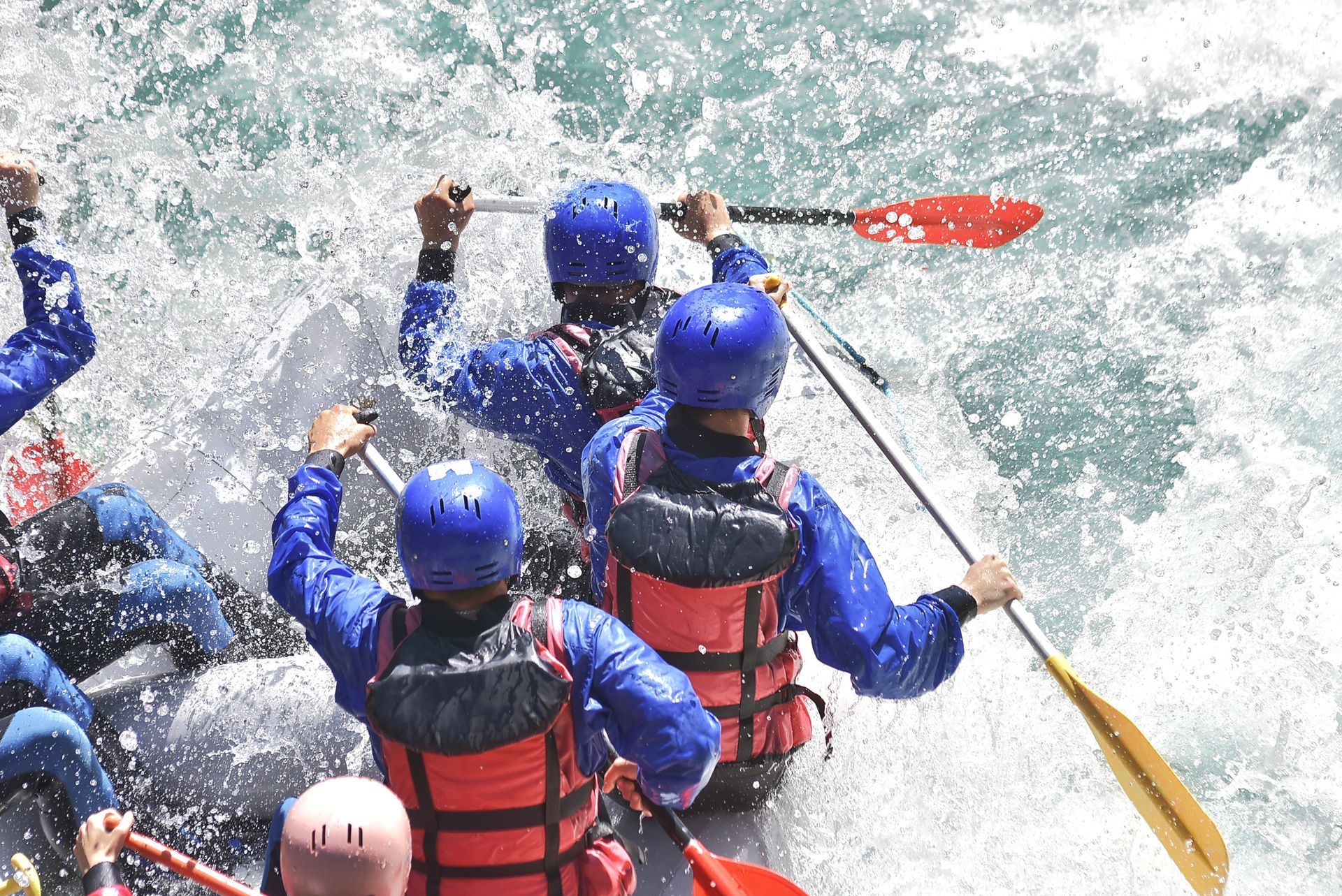People white water rafting through churning, white water rapids; boaters paddling.
