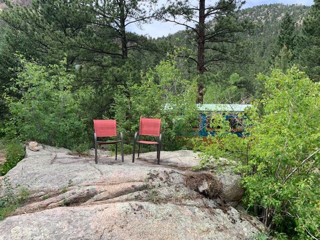 Two red chairs on a rocky outcrop overlook trees and a green and blue structure in a forest.