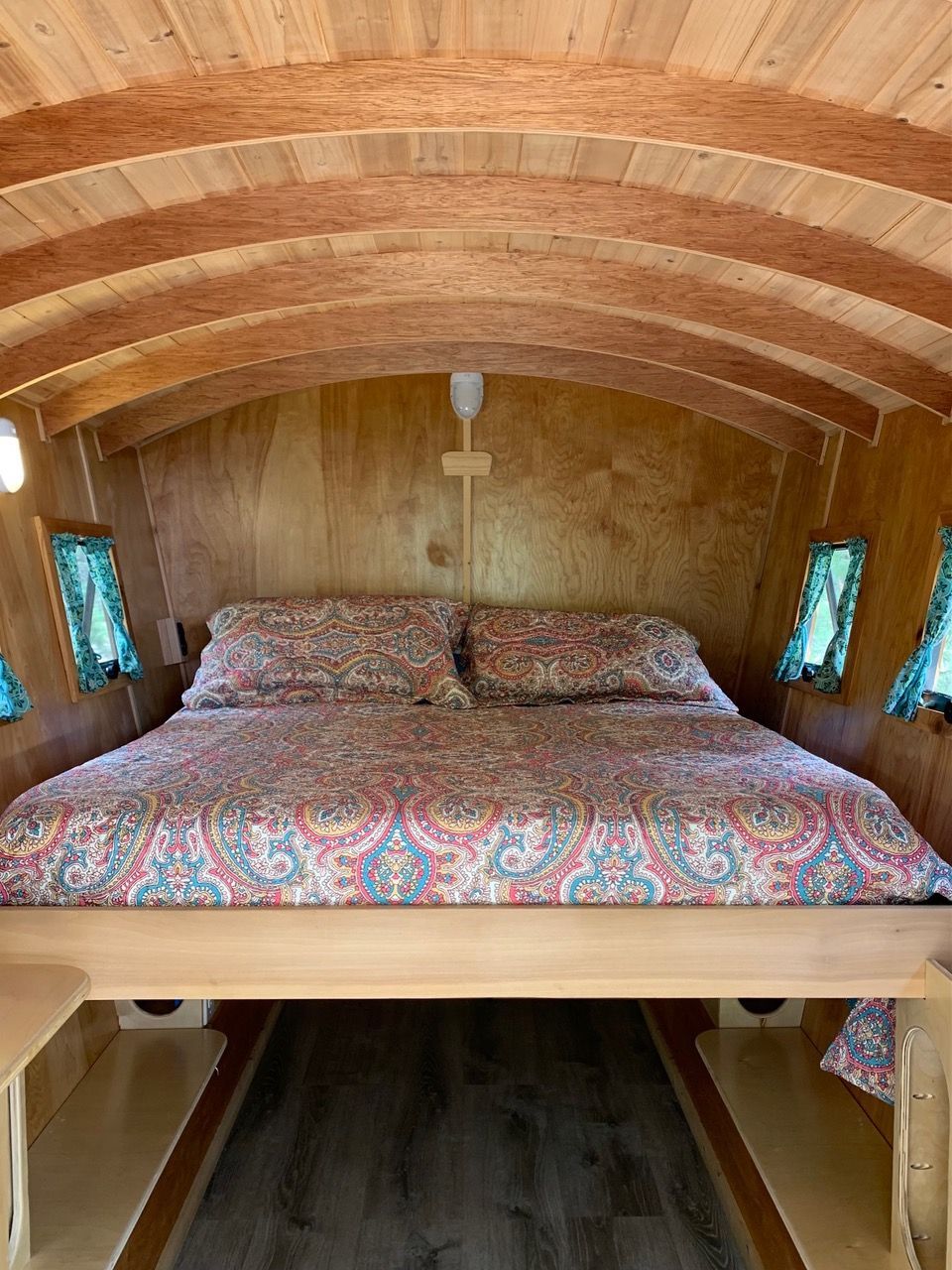 Cozy, wooden tiny home bedroom with a bed, small windows, and arched ceiling.