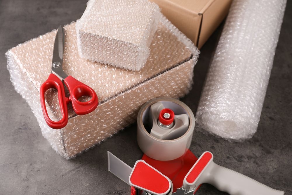A Pair of Scissors Sitting on Top of a Box Next to a Tape Dispenser and Bubble Wrap — AKM Self Storage In Huntlee, NSW