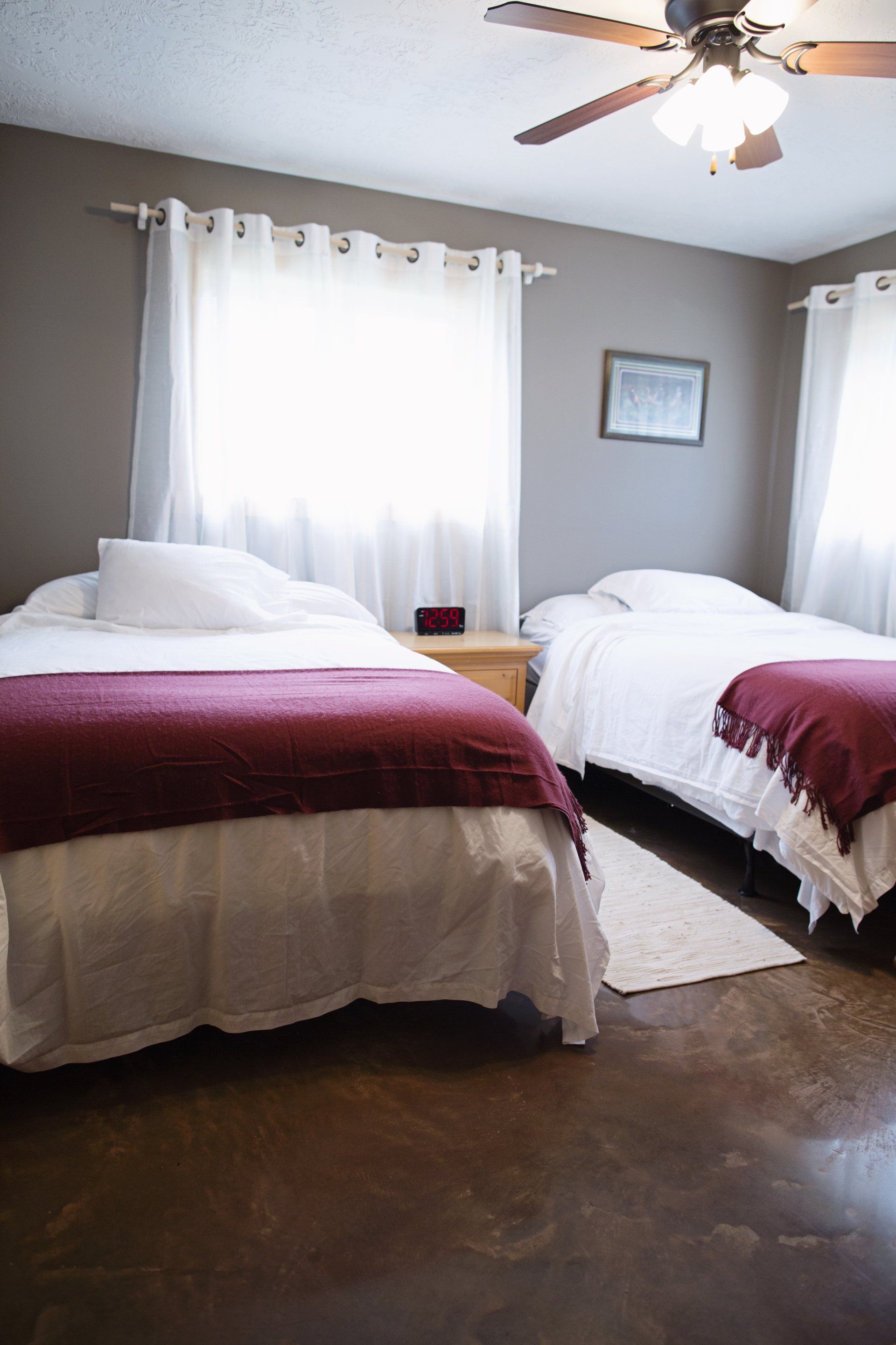 Bedroom with two beds, white curtains, ceiling fan, and gray walls.