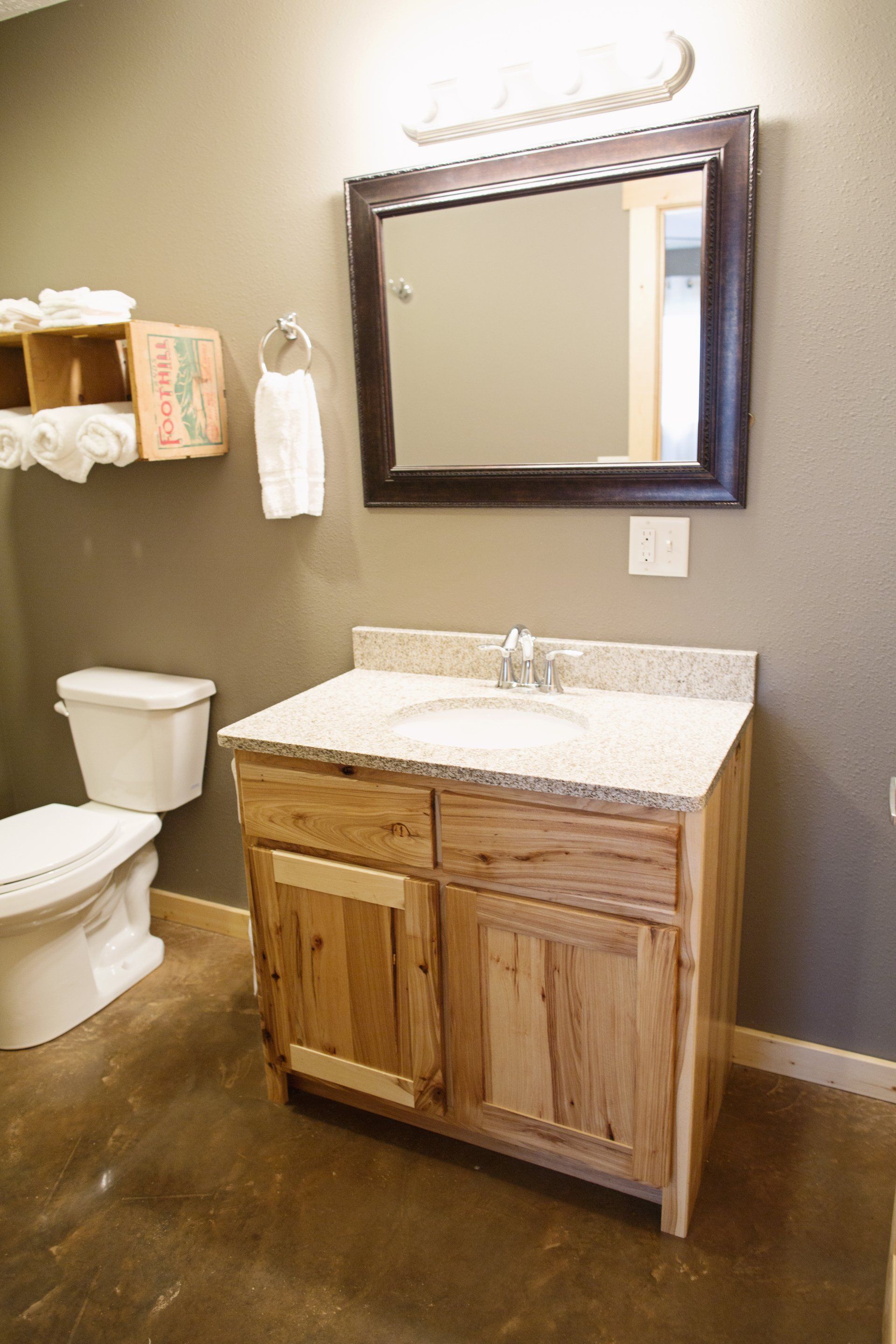 Bathroom vanity with wood cabinet, white sink, mirror, toilet, and gray walls