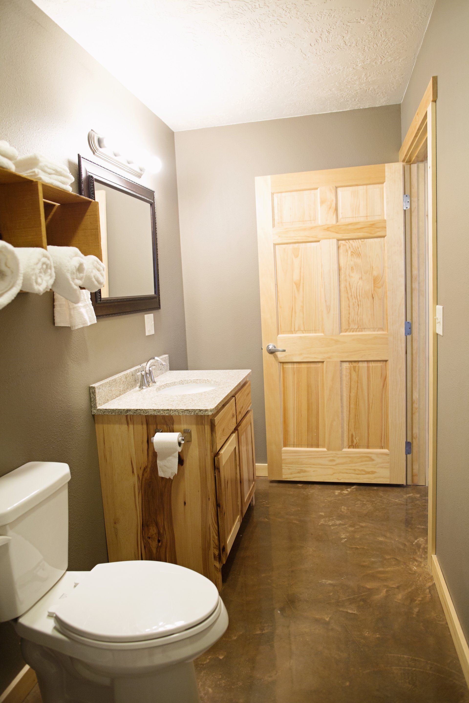 Small bathroom with a toilet, wood vanity, wall mirror, and light wood door.