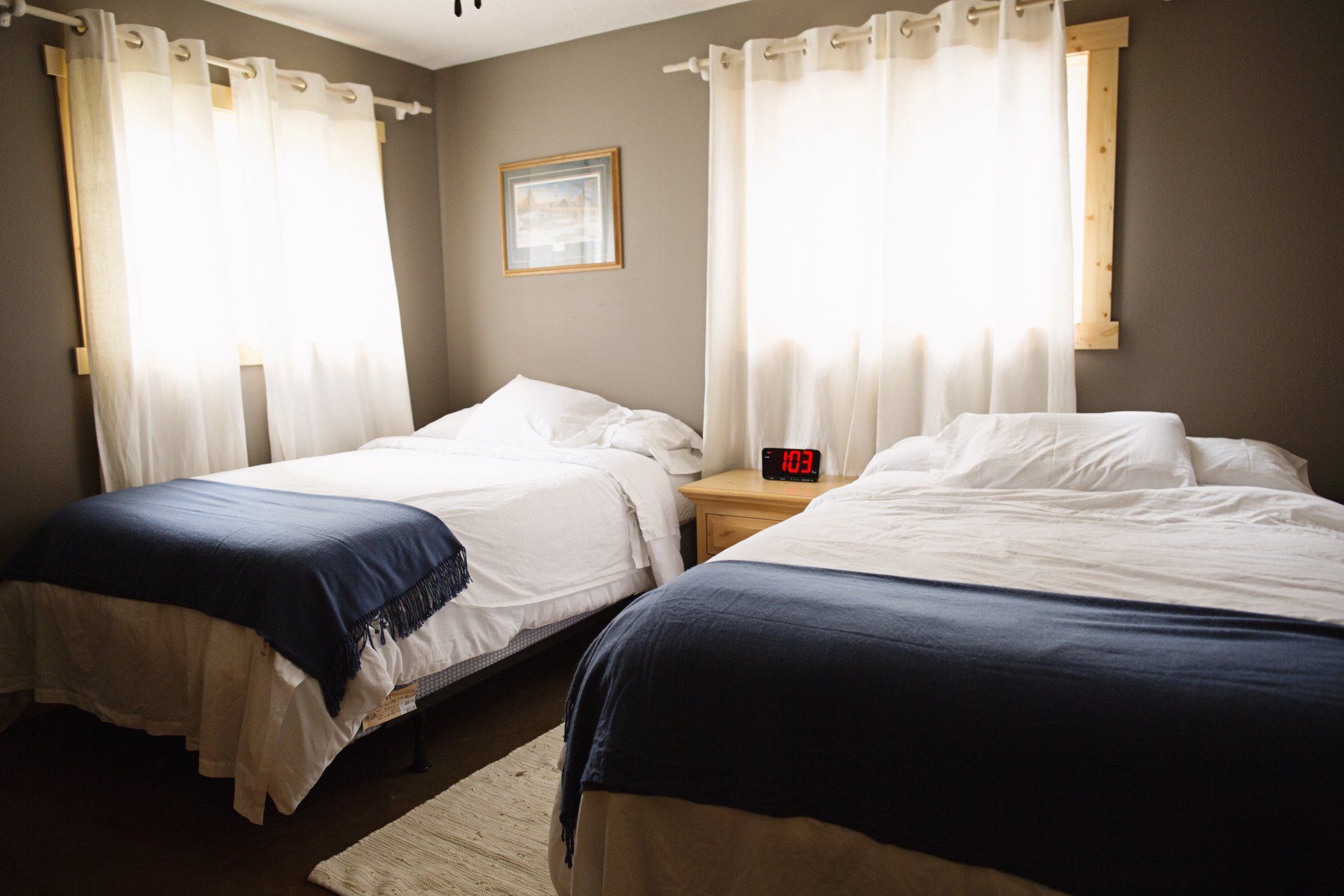 Bedroom with two unmade twin beds, white curtains, and a small wall mirror.