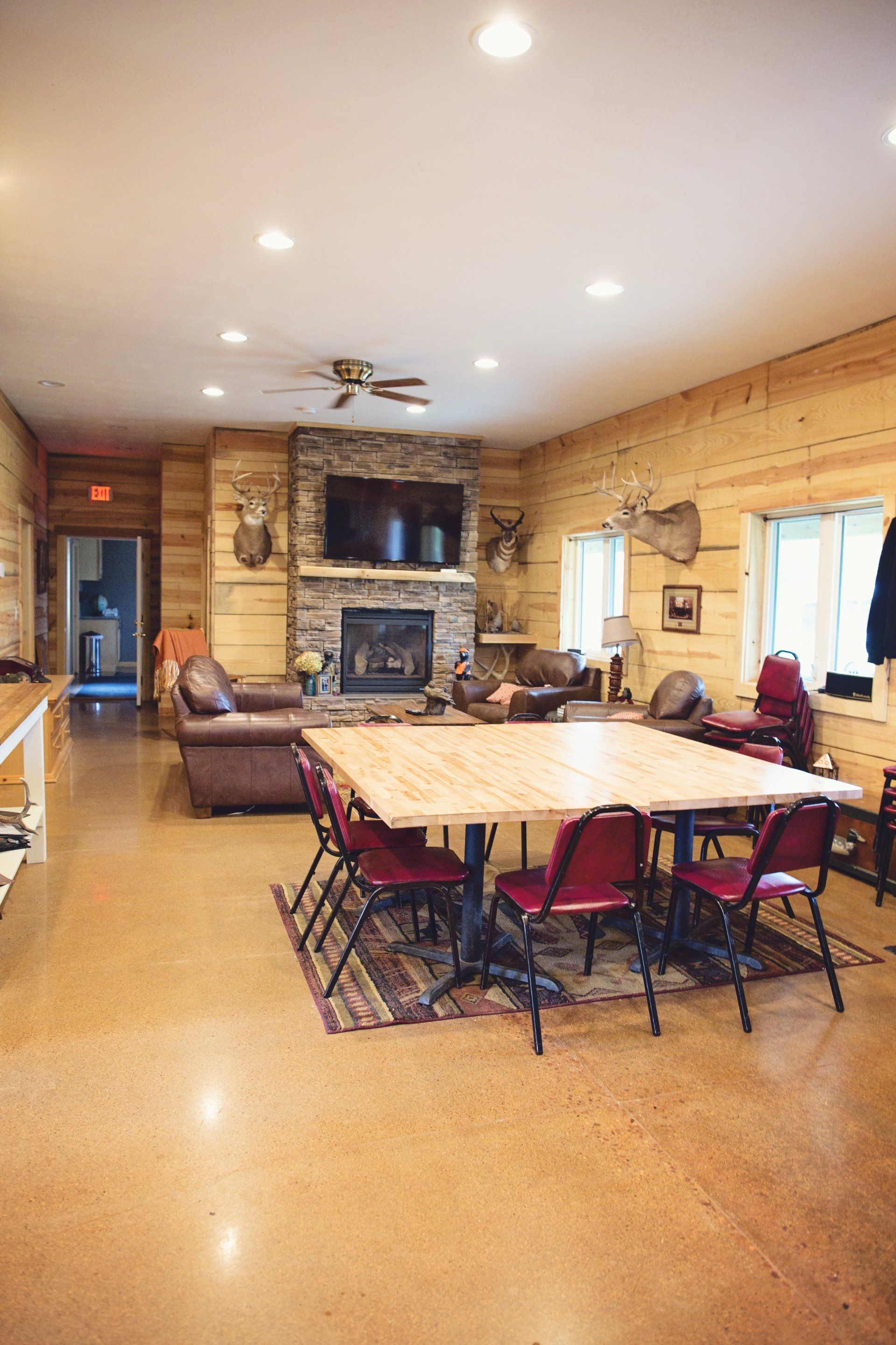 Rustic dining room with wooden walls, stone fireplace, long table, chairs, and recessed lighting