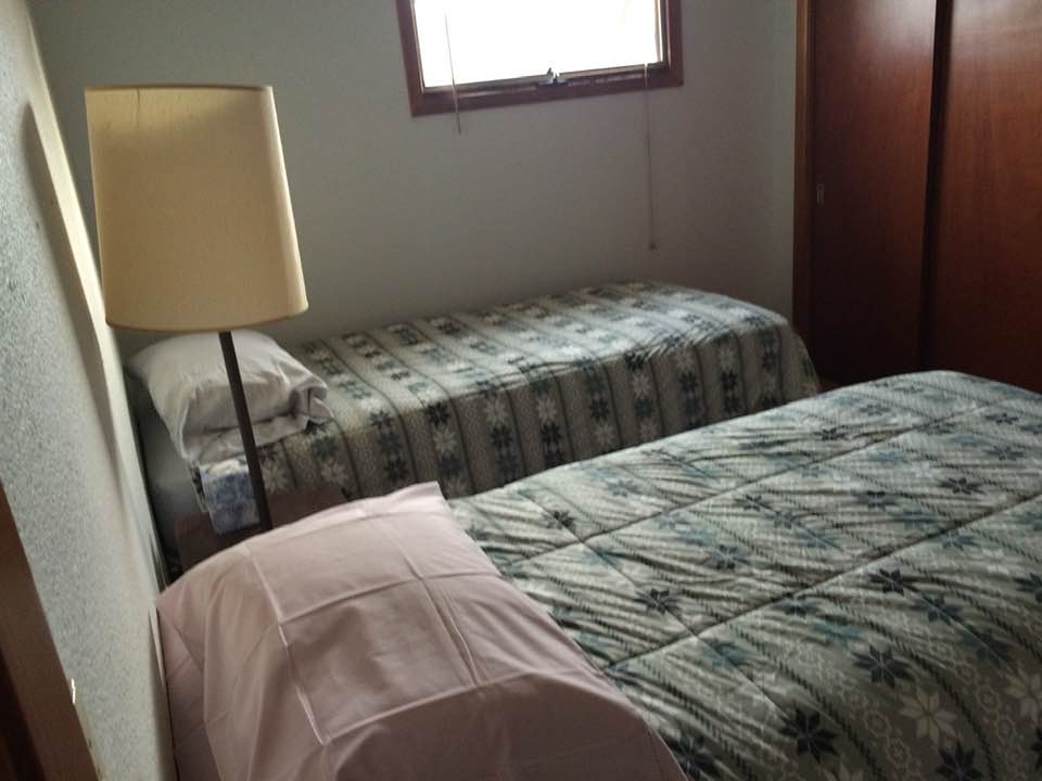 Small bedroom with two patterned beds, a floor lamp, and a window.