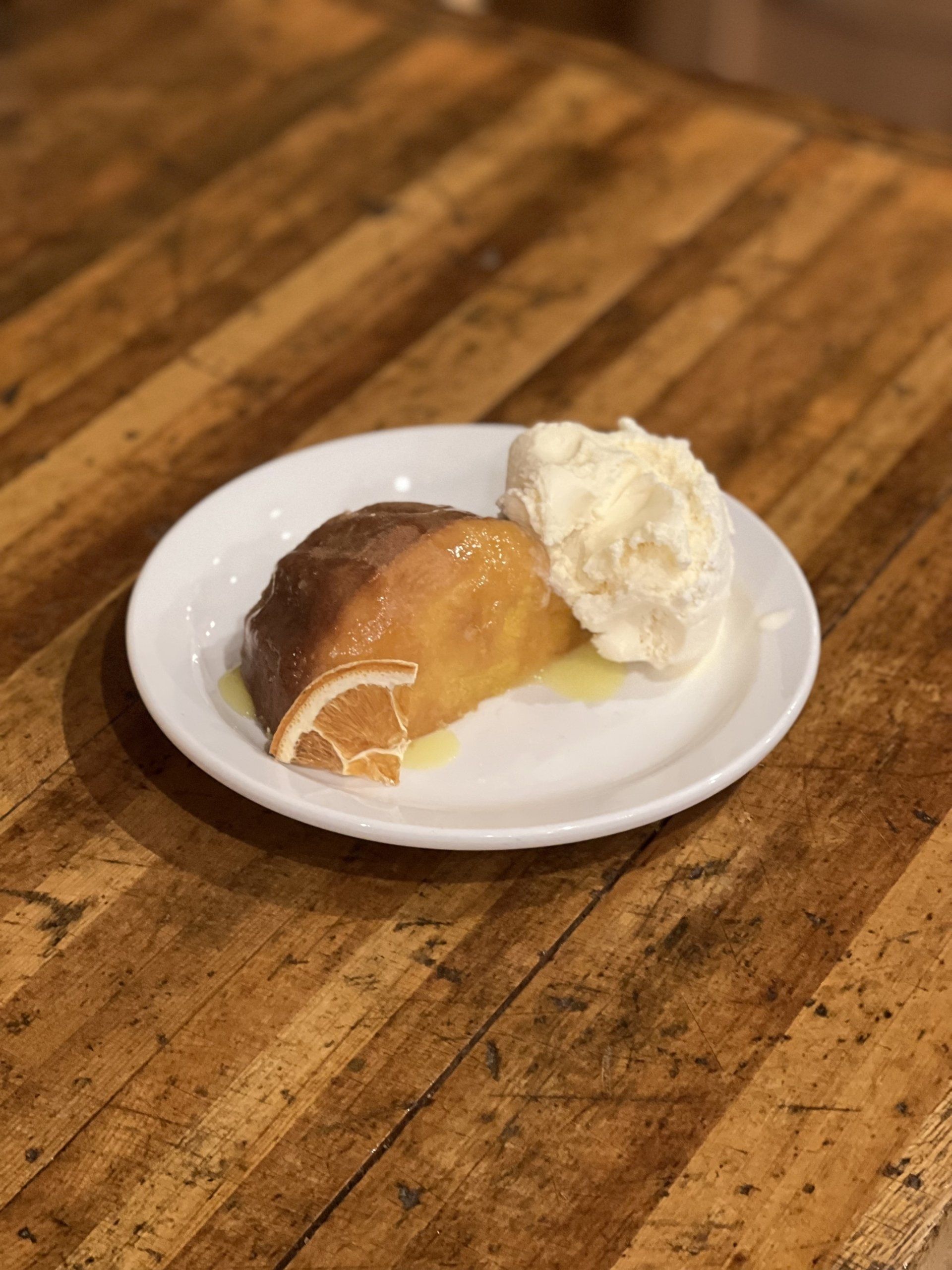 A small dessert on a white plate: chocolate and vanilla ice cream with a caramel pastry on a wooden table.