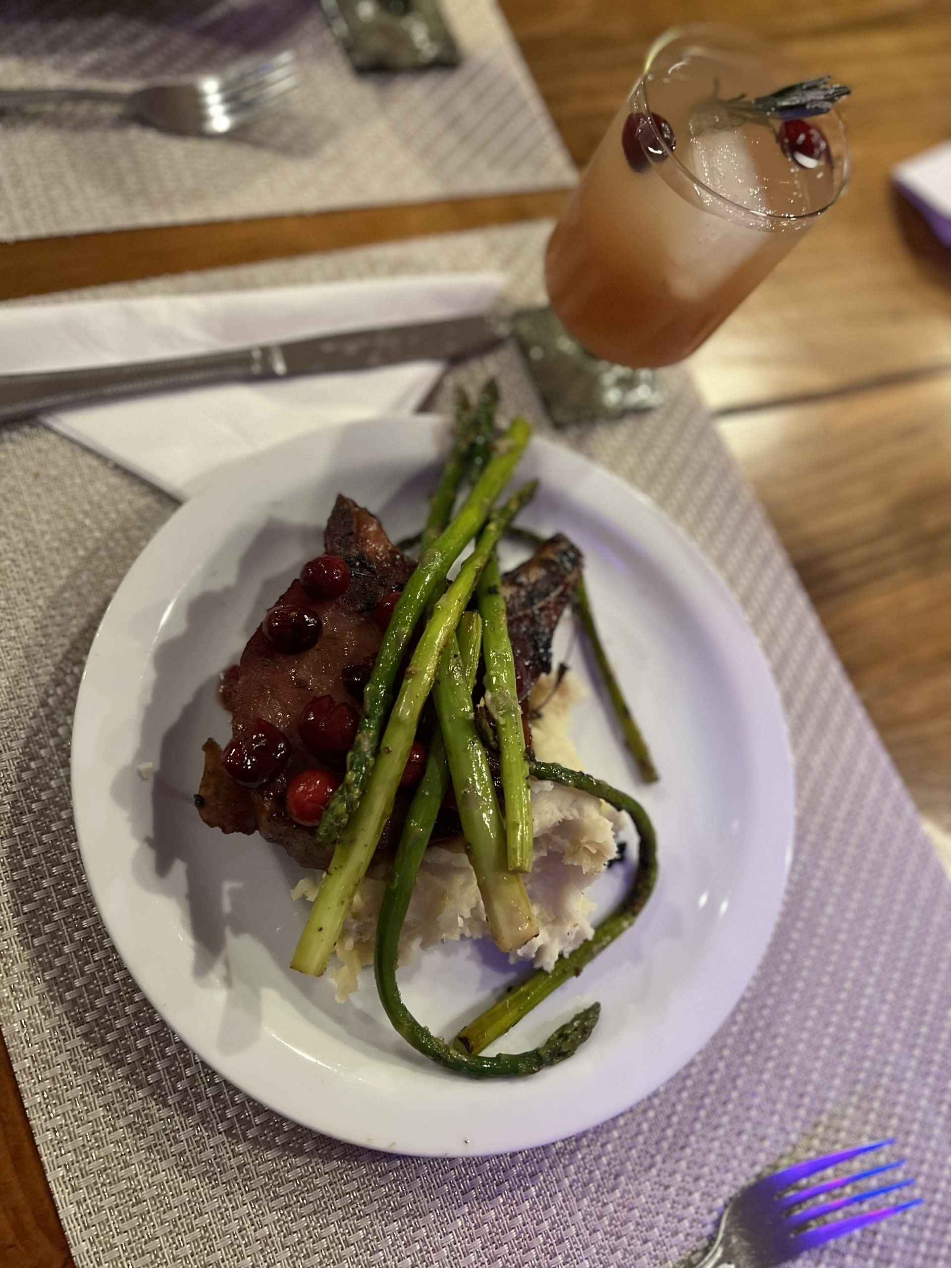 Plated steak with asparagus on a restaurant table, with a cocktail beside it.