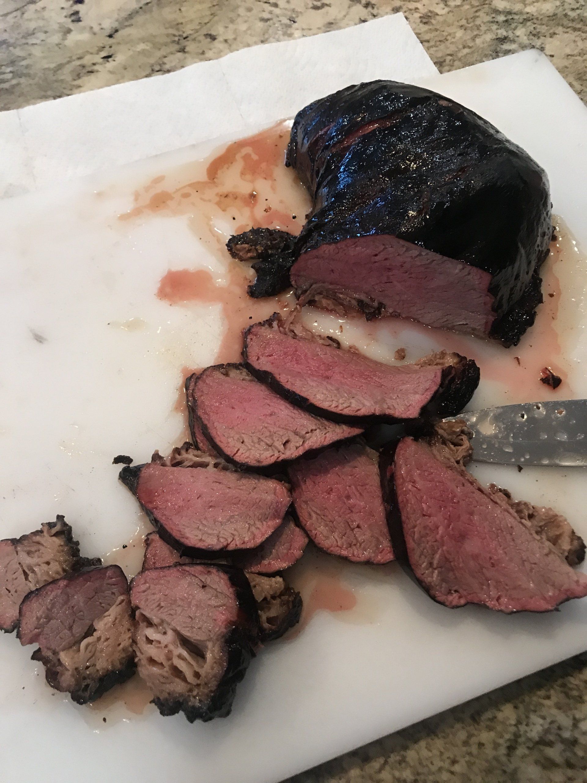 Sliced smoked meat with pink center on a cutting board, with a dark crust on top