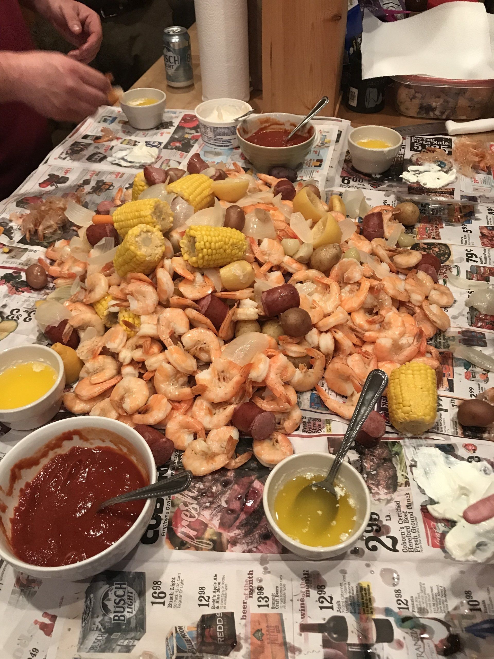 Seafood boil spread with shrimp, corn, potatoes, and dipping sauces on a newspaper-covered table