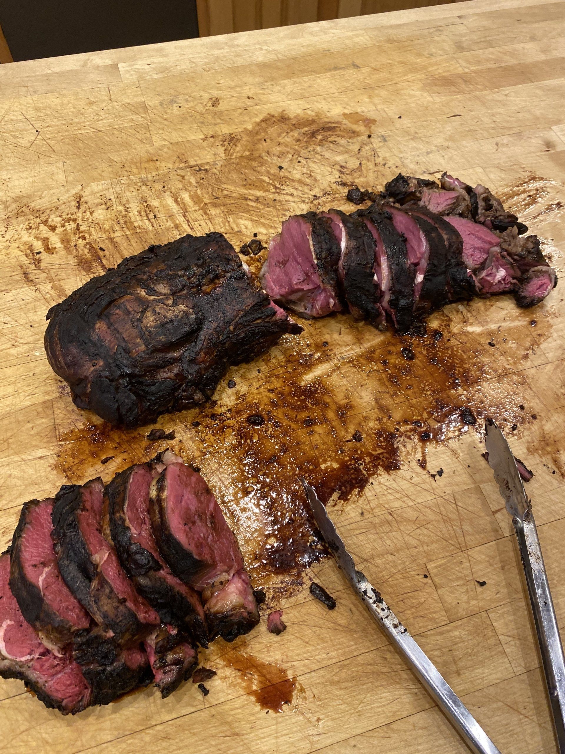 Sliced medium-rare steak on a cutting board with a carving knife and meat juices.