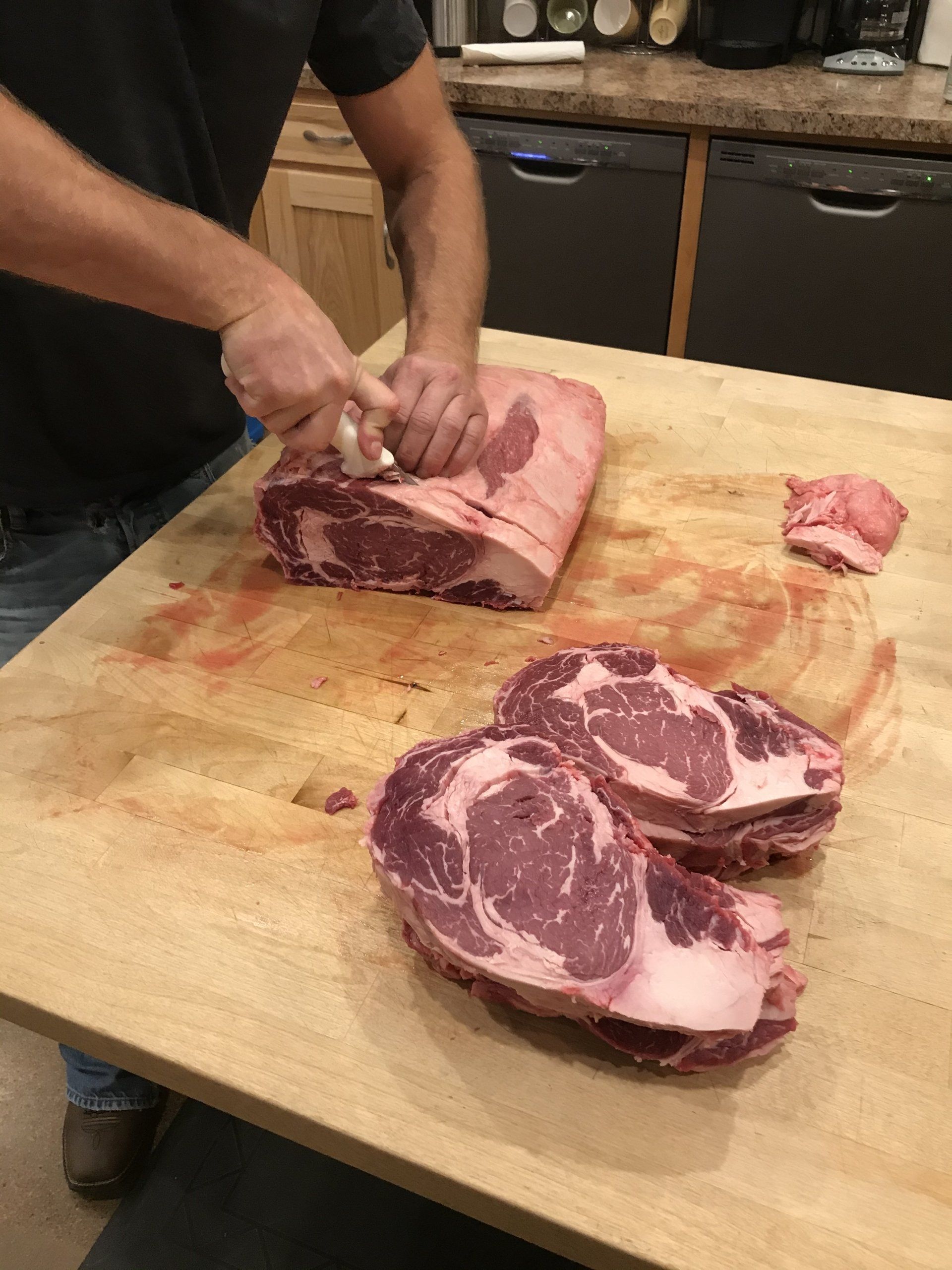 Butcher slicing a large raw beef roast on a wooden cutting board in a kitchen