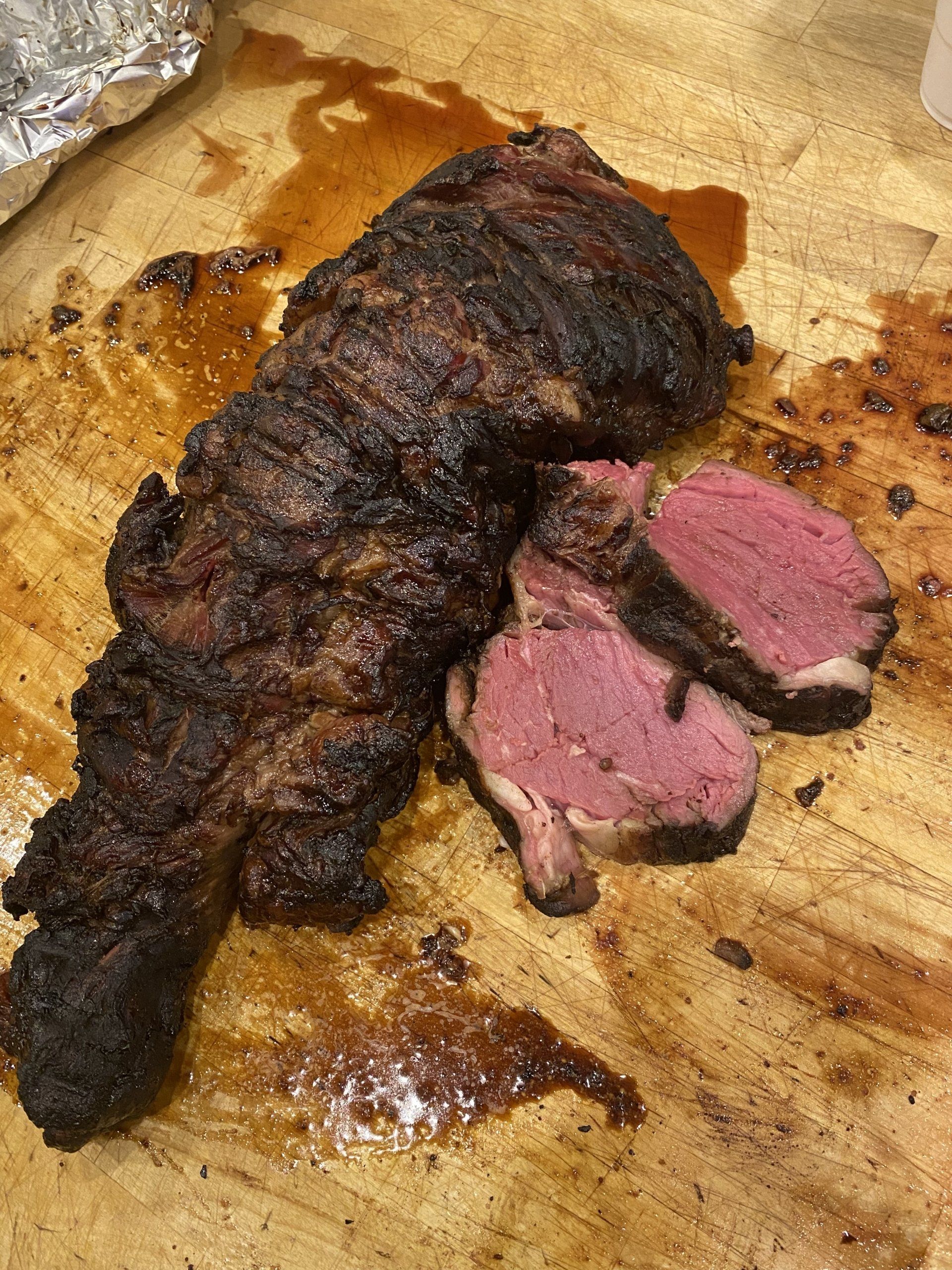 Sliced medium-rare steak on a wooden cutting board, with a dark seared crust and pink center.