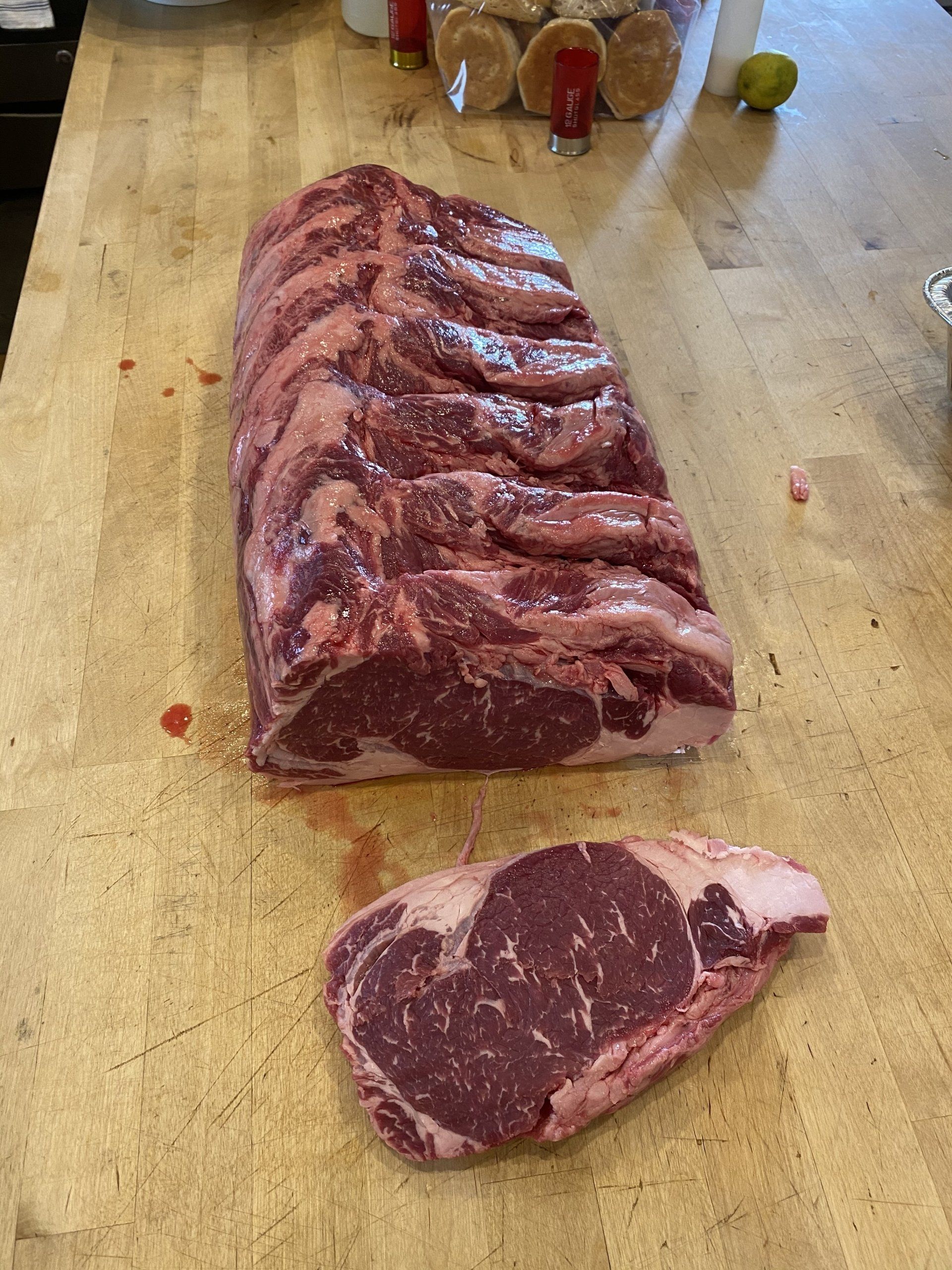 Raw marbled beef roast cut into steaks on a wooden cutting board, with one slice in front
