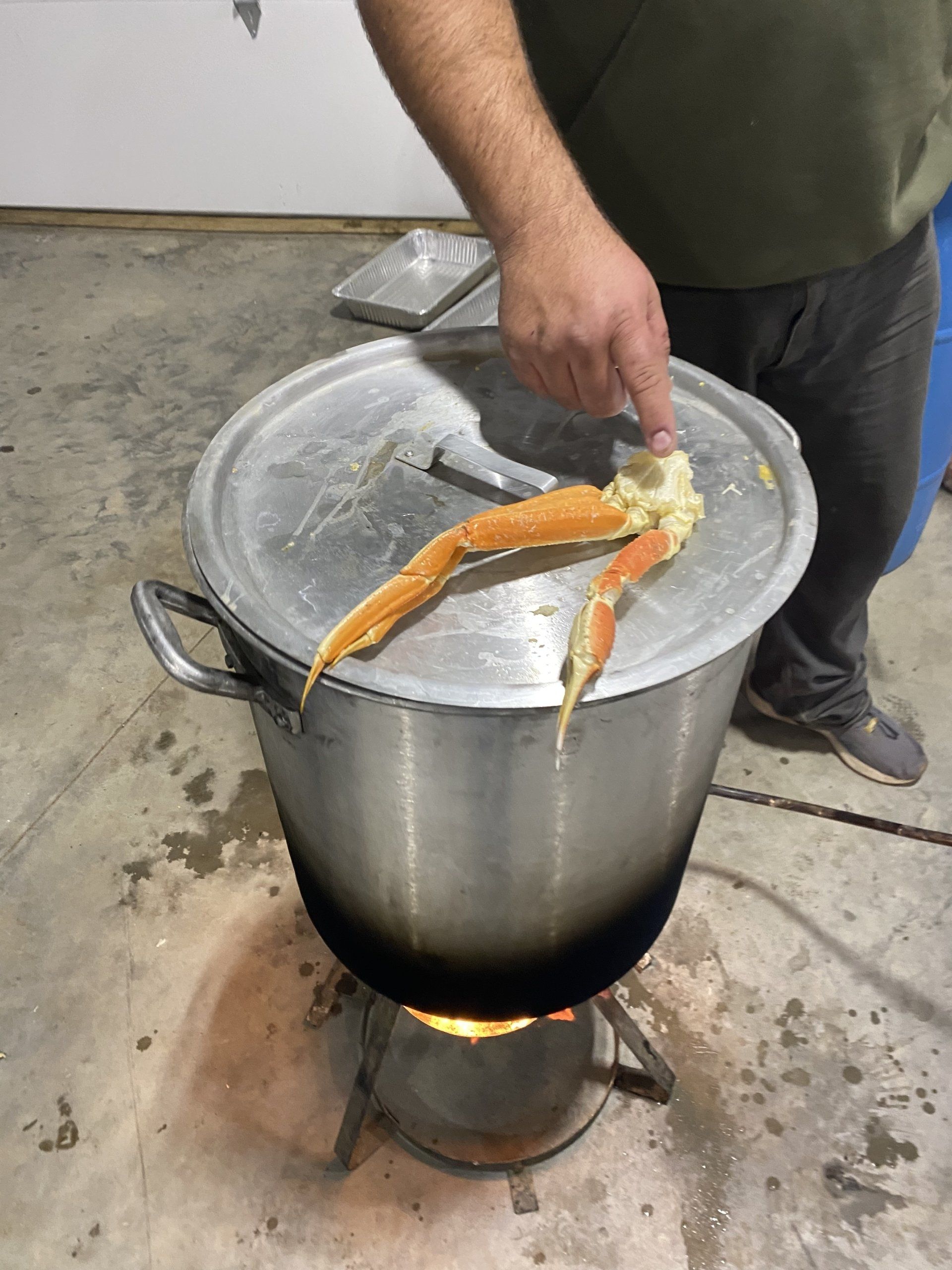 Large pot boiling over a flame as a person stirs orange fish on the lid in a kitchen setting
