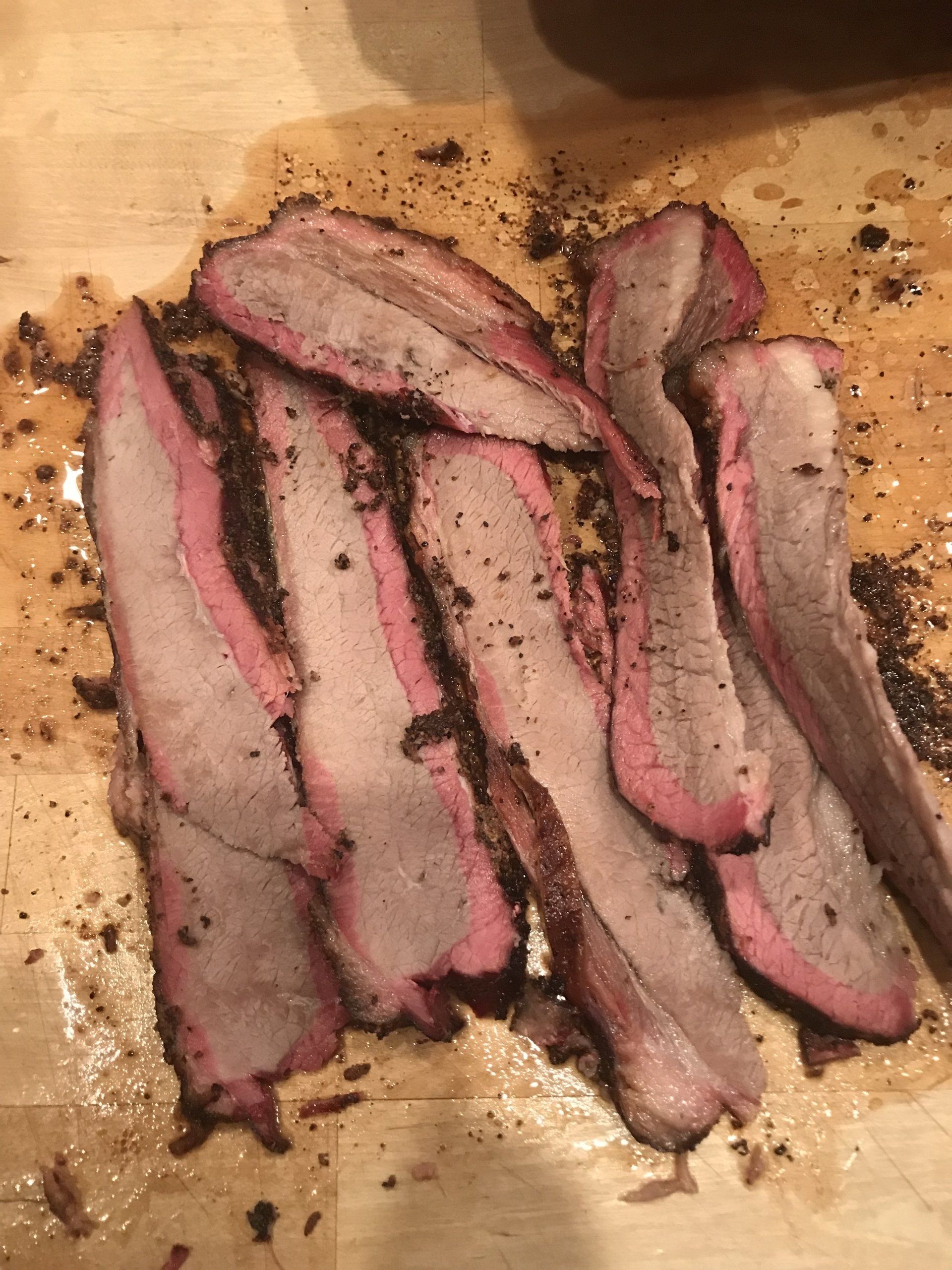 Sliced smoked beef on a wooden cutting board, with dark peppered edges and pink centers