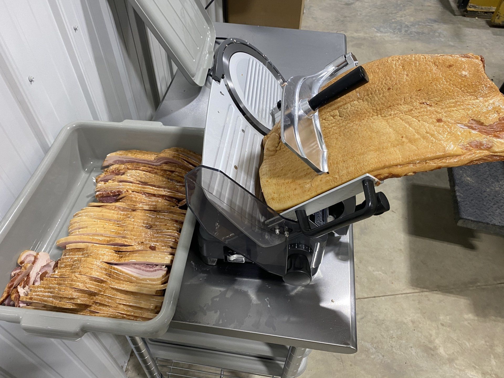 Tray and slicer machine in a kitchen, with stacks of sliced bread on a gray counter.