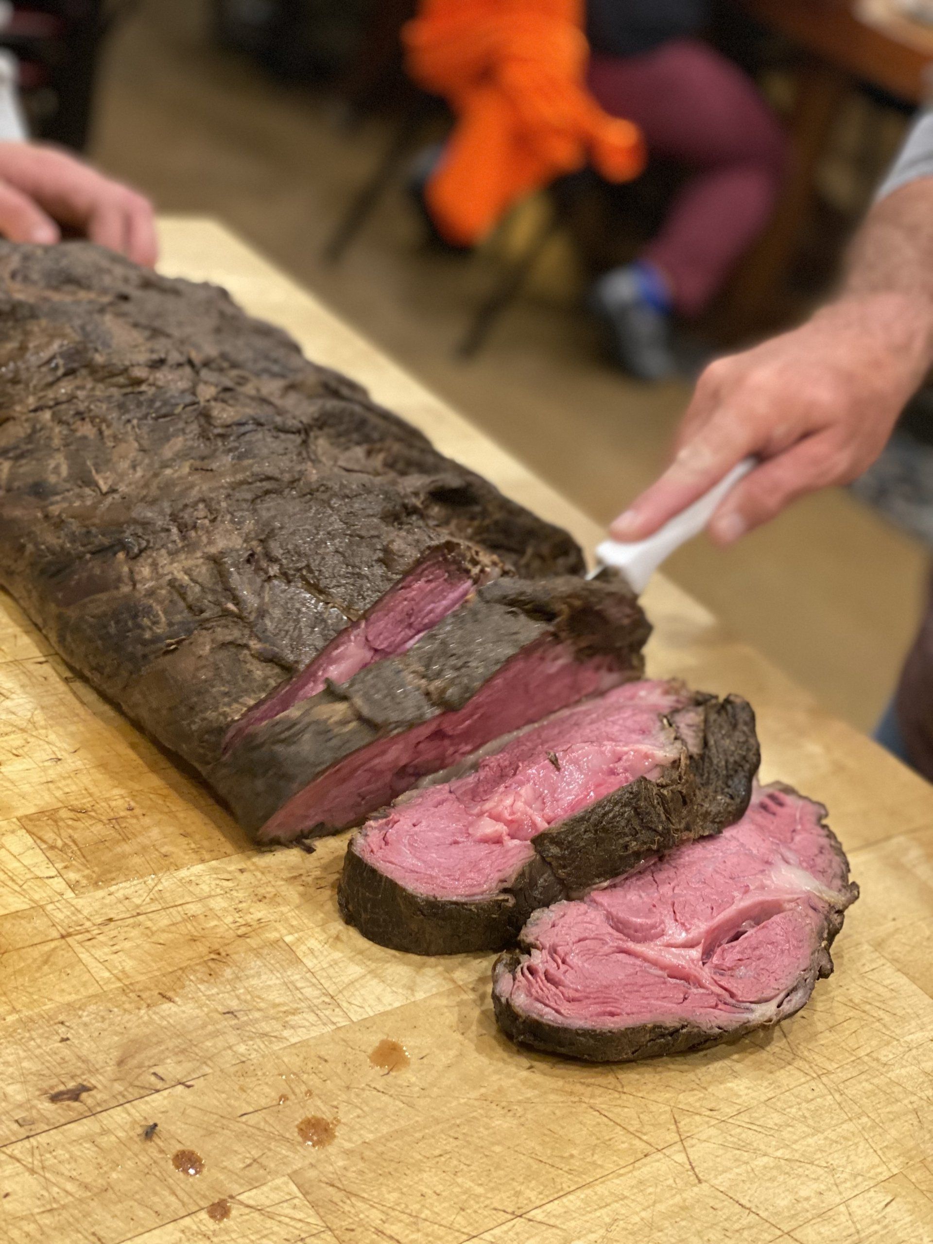Slices of medium-rare roast beef being carved on a wooden cutting board