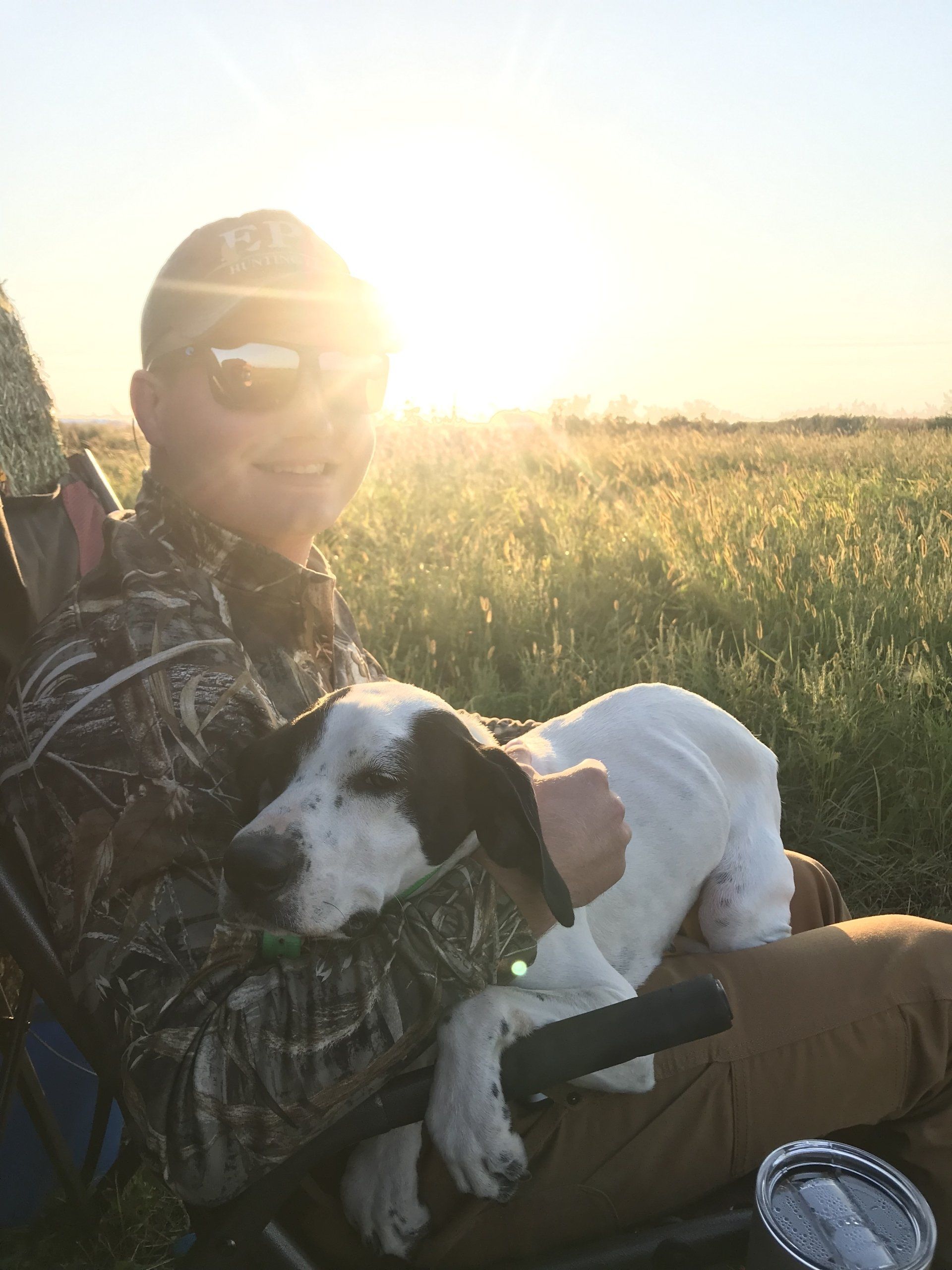 Person holding a black-and-white dog in a sunny field at sunset