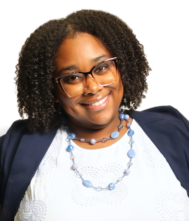 Smiling person with curly hair, glasses, navy blazer, and blue necklace against a white background