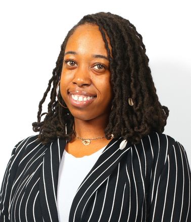 Portrait of a smiling person with long braids, wearing a black striped blazer over a white top.