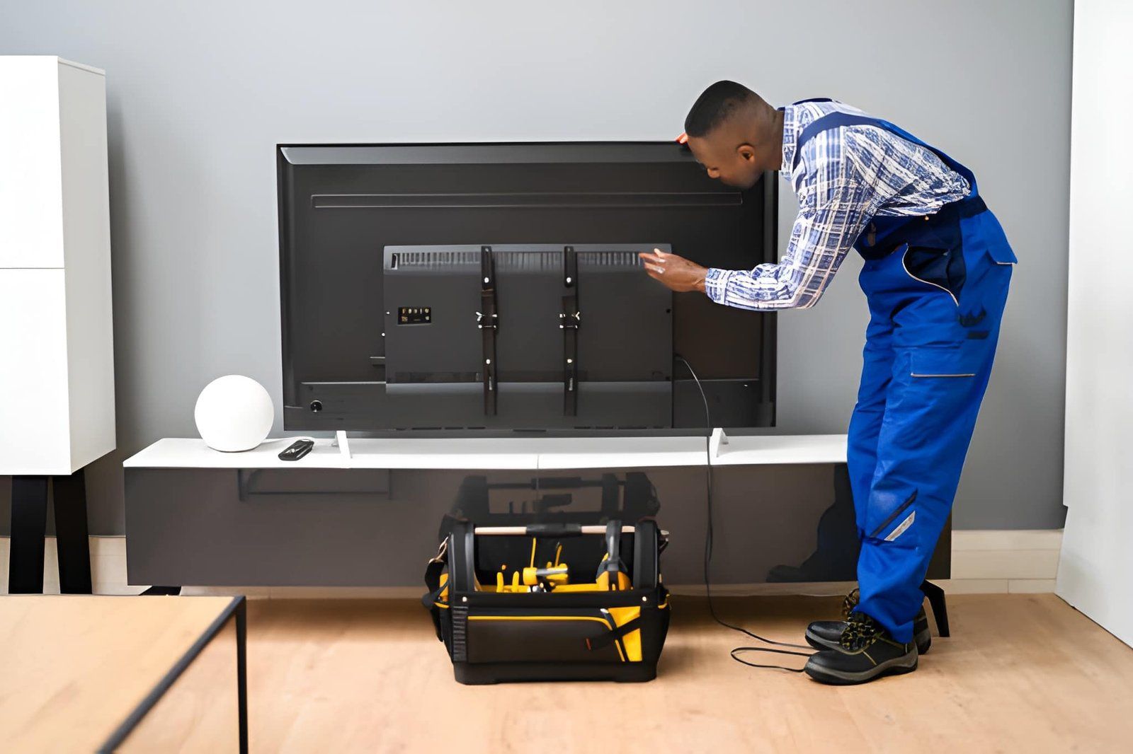 Technician in blue overalls adjusting a wall-mounted TV in a modern room