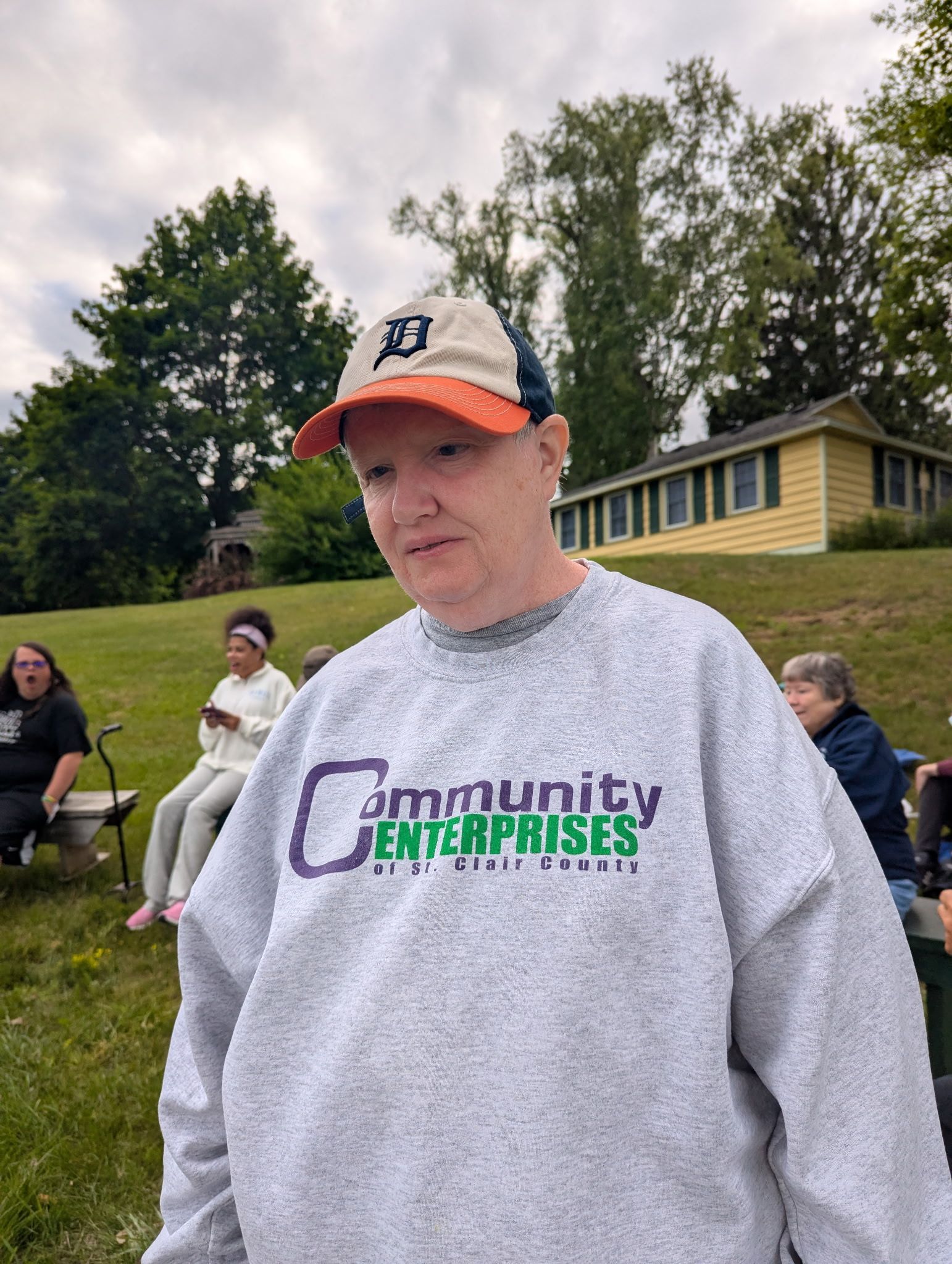 A person wearing a baseball cap and sweatshirt stands outside near other people.