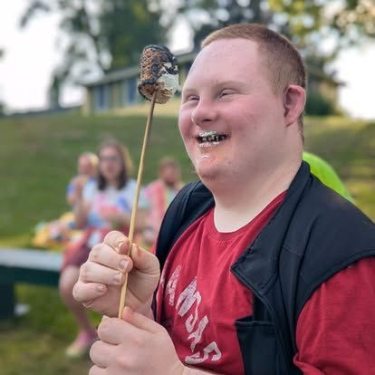 Smiling person with Down syndrome eating a roasted marshmallow outdoors.