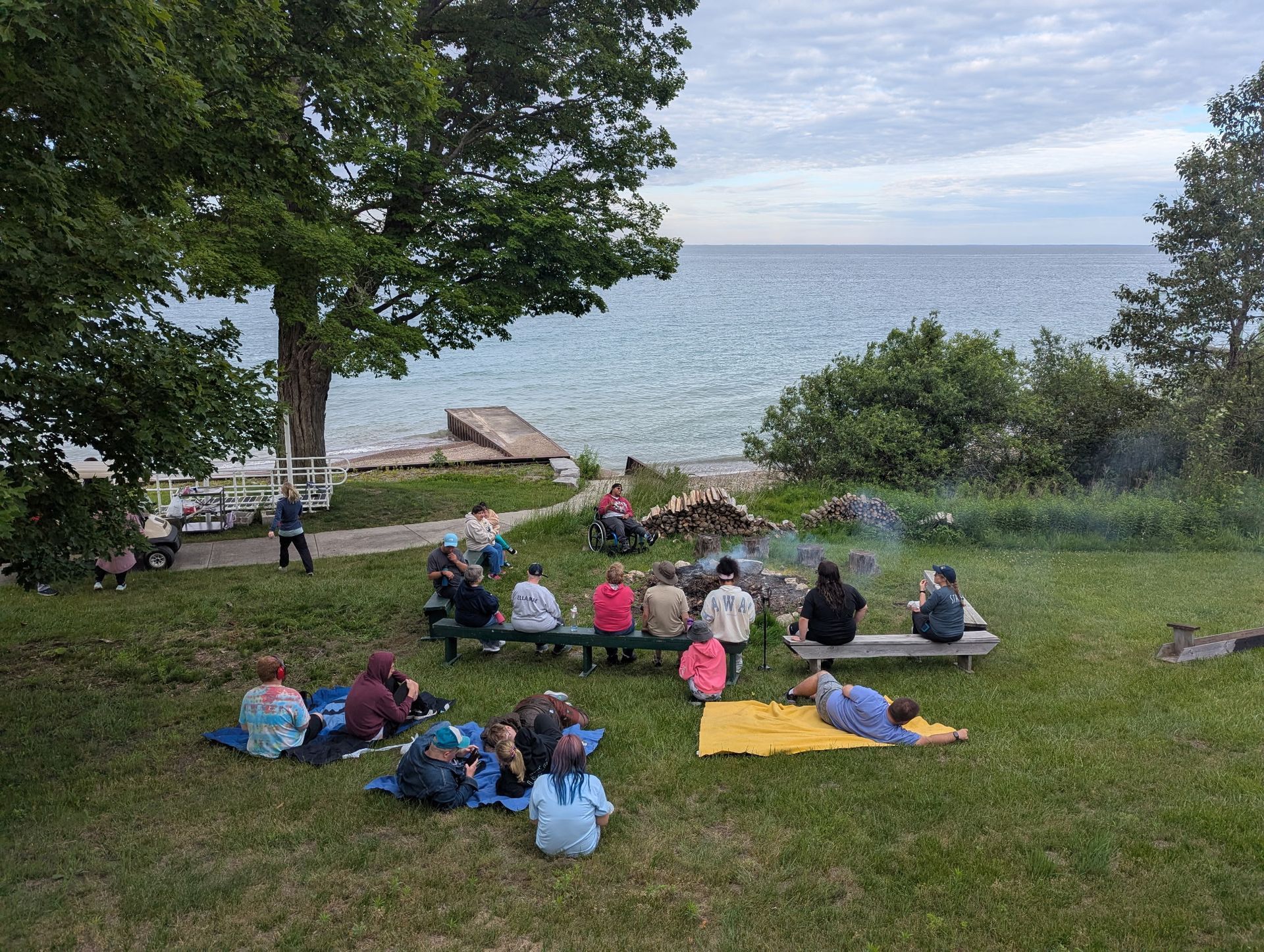 People gathered around a campfire near a lake under an overcast sky.