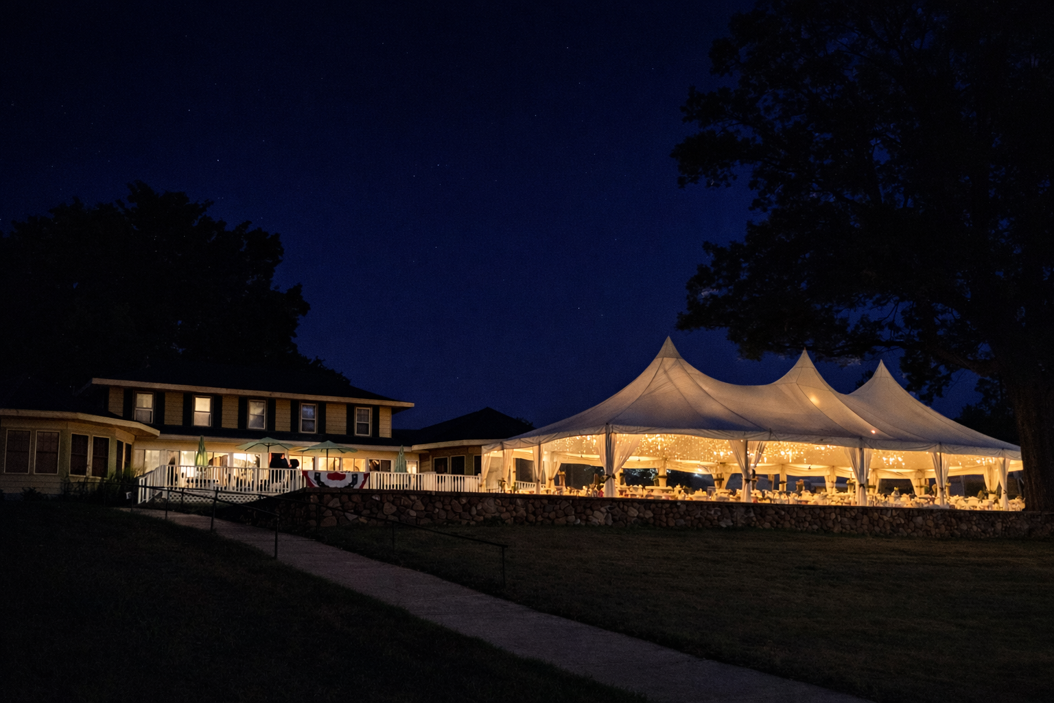 Nighttime view: lit event tent and building against dark sky. Pathway in foreground.